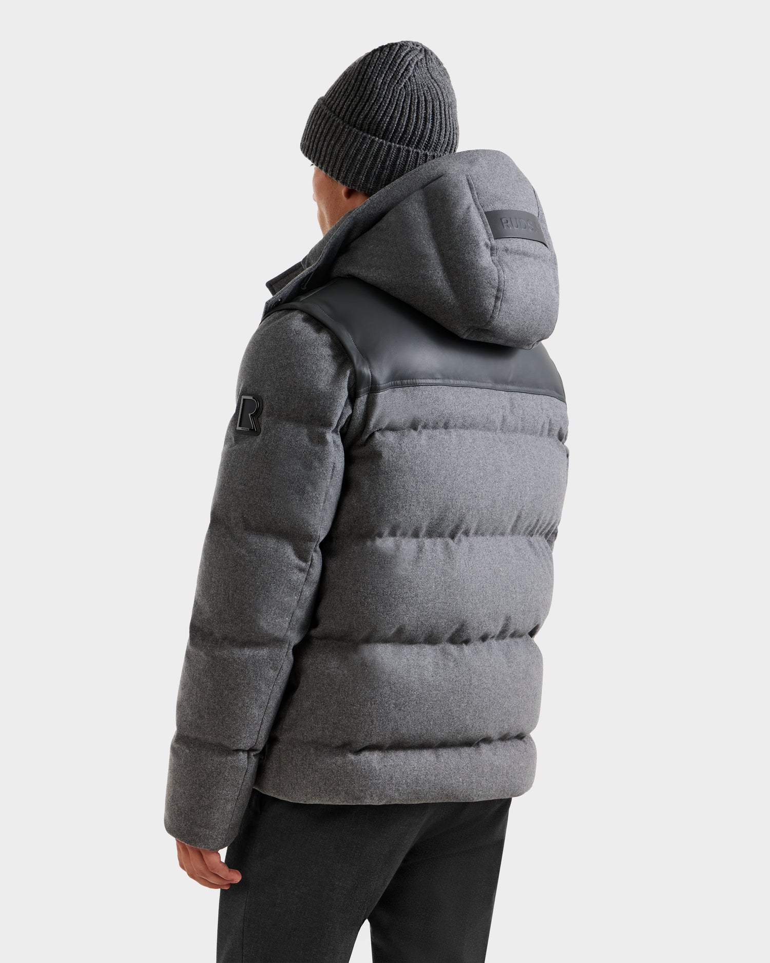 A person is seen from the back against a plain light background wearing the Rudsak BALDWIN W - 6125532 Heather Charcoal men’s down parka with a hood and a gray beanie—a true winter staple.