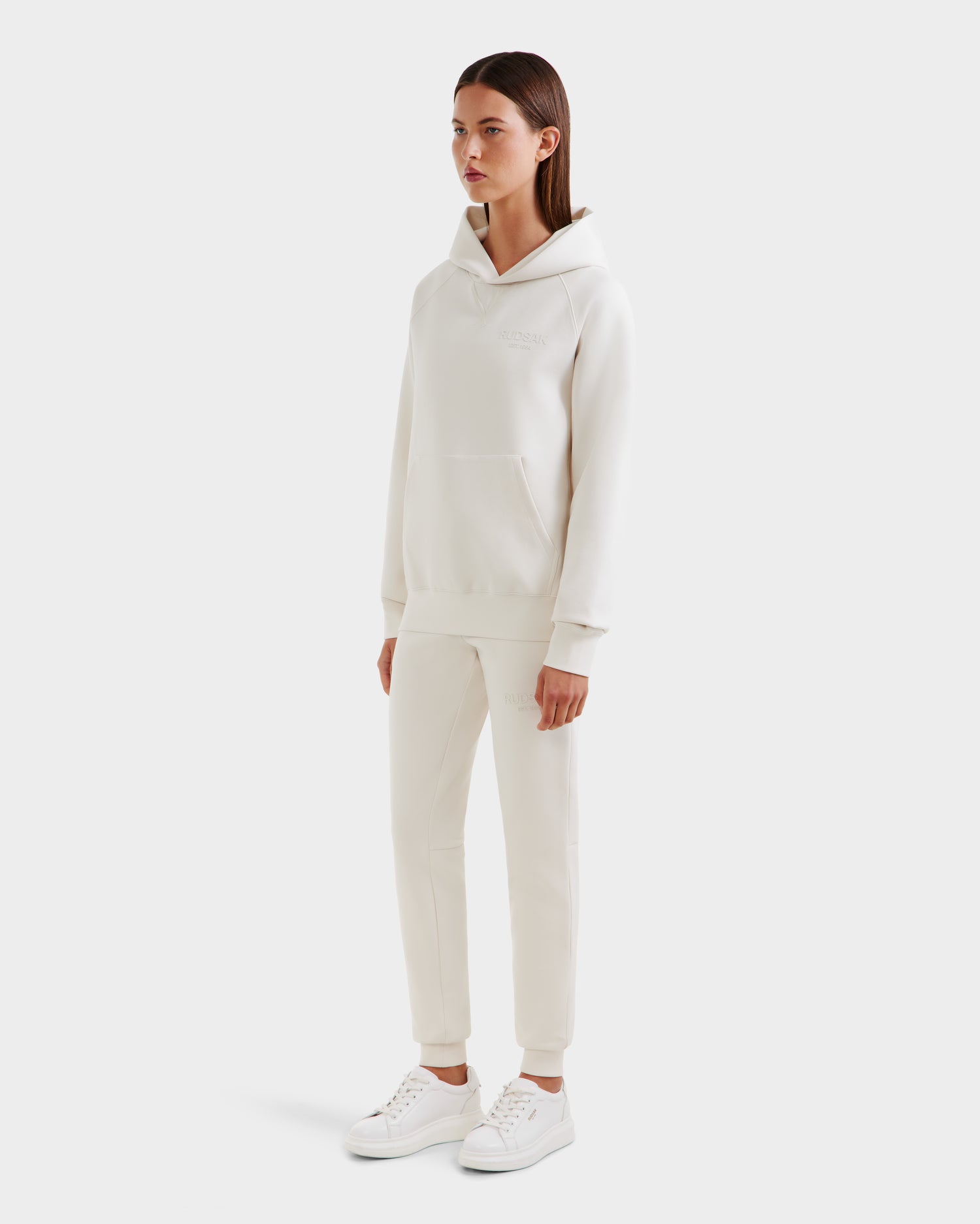 A person poses against a white background wearing Rudsak's BARRY - 9524011 Vanilla W hoodie and sweatpants set. The oversized, unisex fit embodies effortless casual style inspired by the signature Rudsak collection.