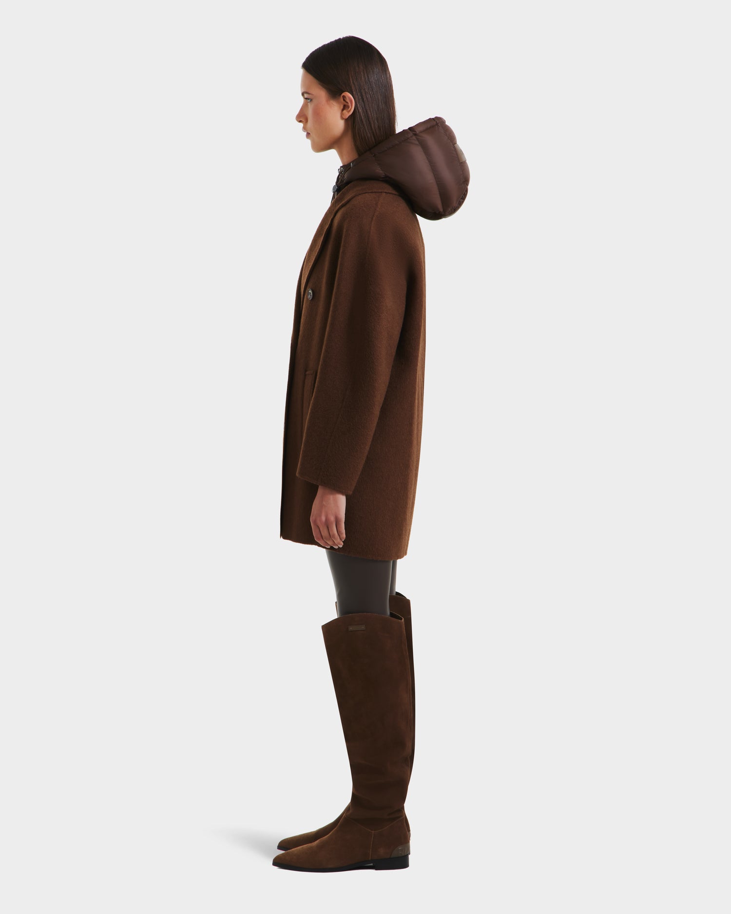 A woman in profile models the Rudsak BETHANY - 8125625 Mocha modular outerwear coat with a large hood, paired with dark leggings and knee-high brown boots against a plain white background.