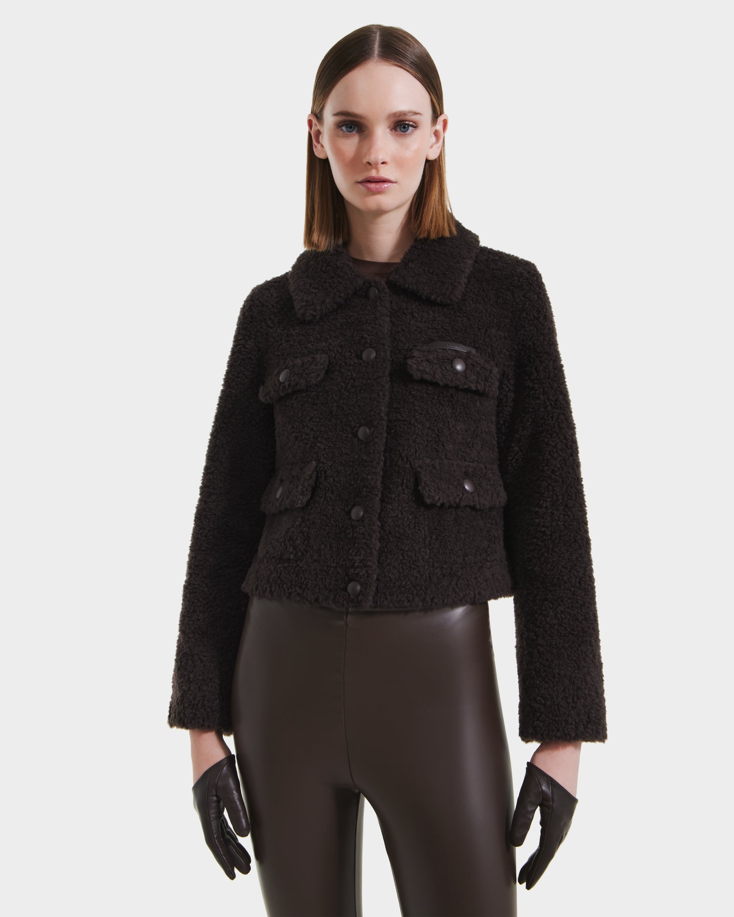 A woman faces forward wearing the Rudsak BLAIR - 8125513 Espresso jacket, brown faux leather pants, and black gloves against a plain white background.
