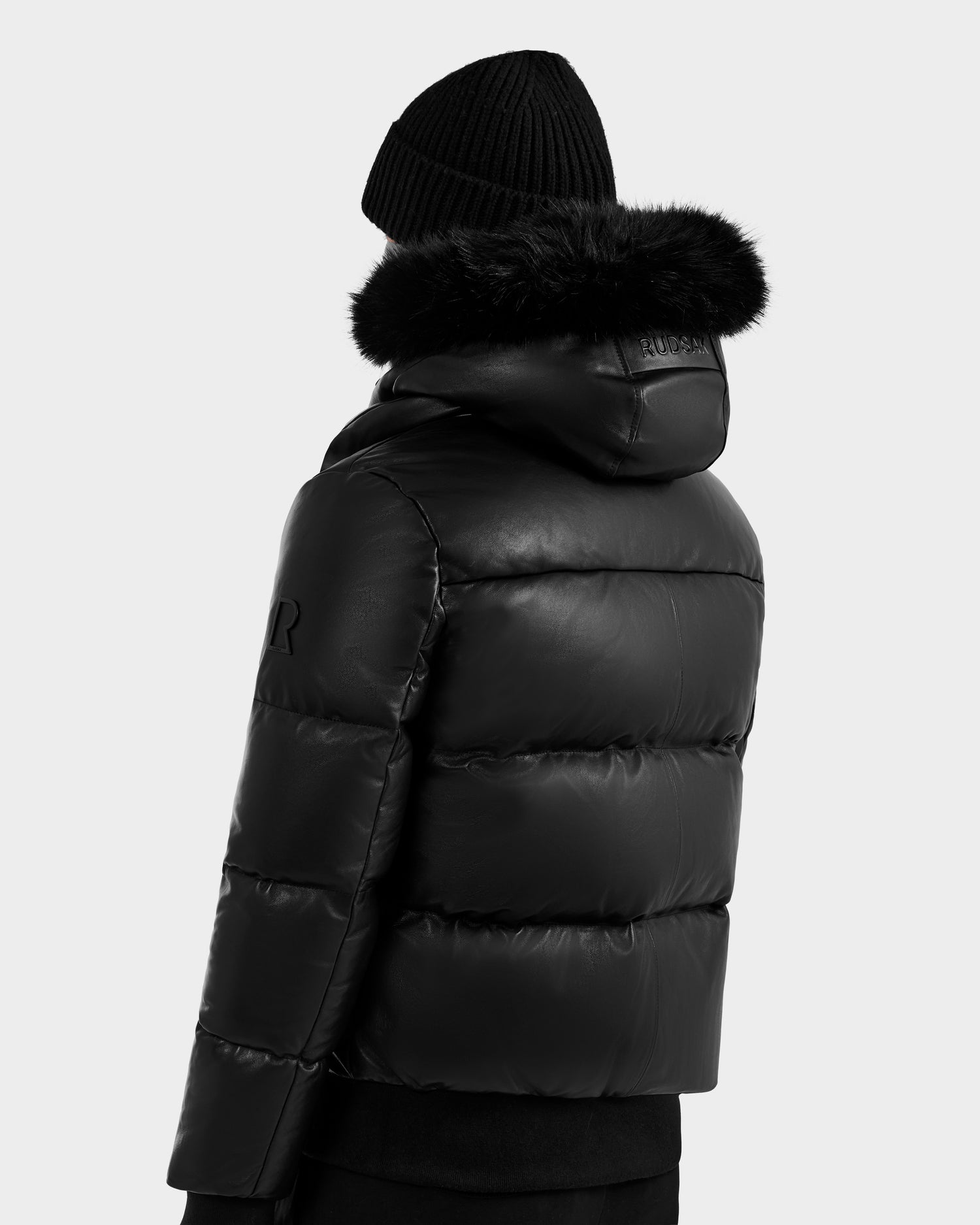 A person shown from the back, wearing the RUDSAK BOND X - 6122525 BLACK men's winter jacket with a fur-lined hood and a black knit beanie, set against a plain light gray background.