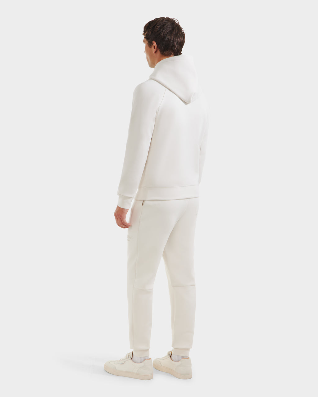 A person stands facing away, wearing the Rudsak BROOKLYN - 6525593 Vanilla hoodie and jogger set, paired with white sneakers against a plain light background.