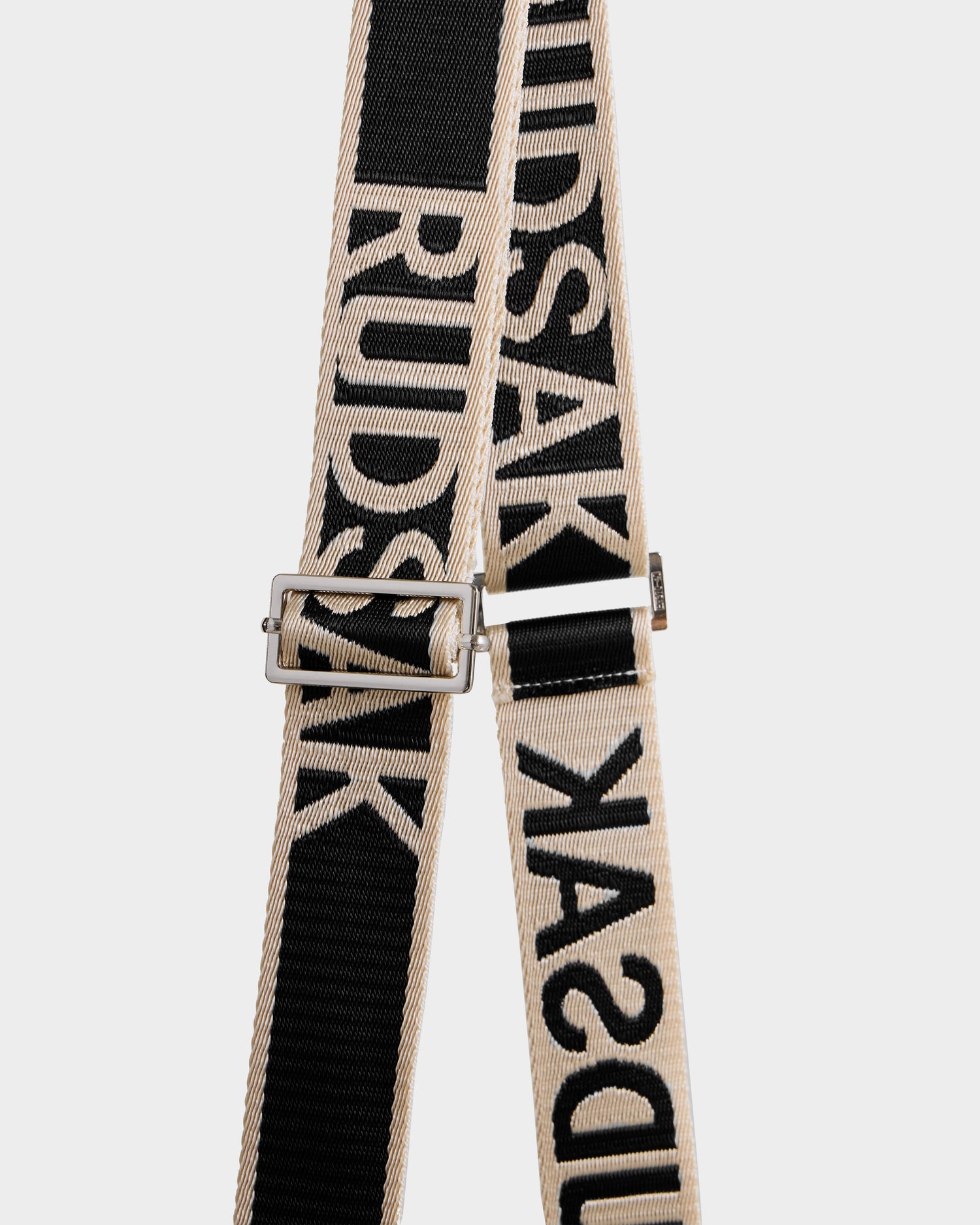 Close-up of the Rudsak CABAS - 8325545 Black’s black and beige strap with bold "RUDSAK" lettering and a silver adjustable buckle—an eye-catching accessory that elevates any faux fur mini tote, pictured on a plain white background.