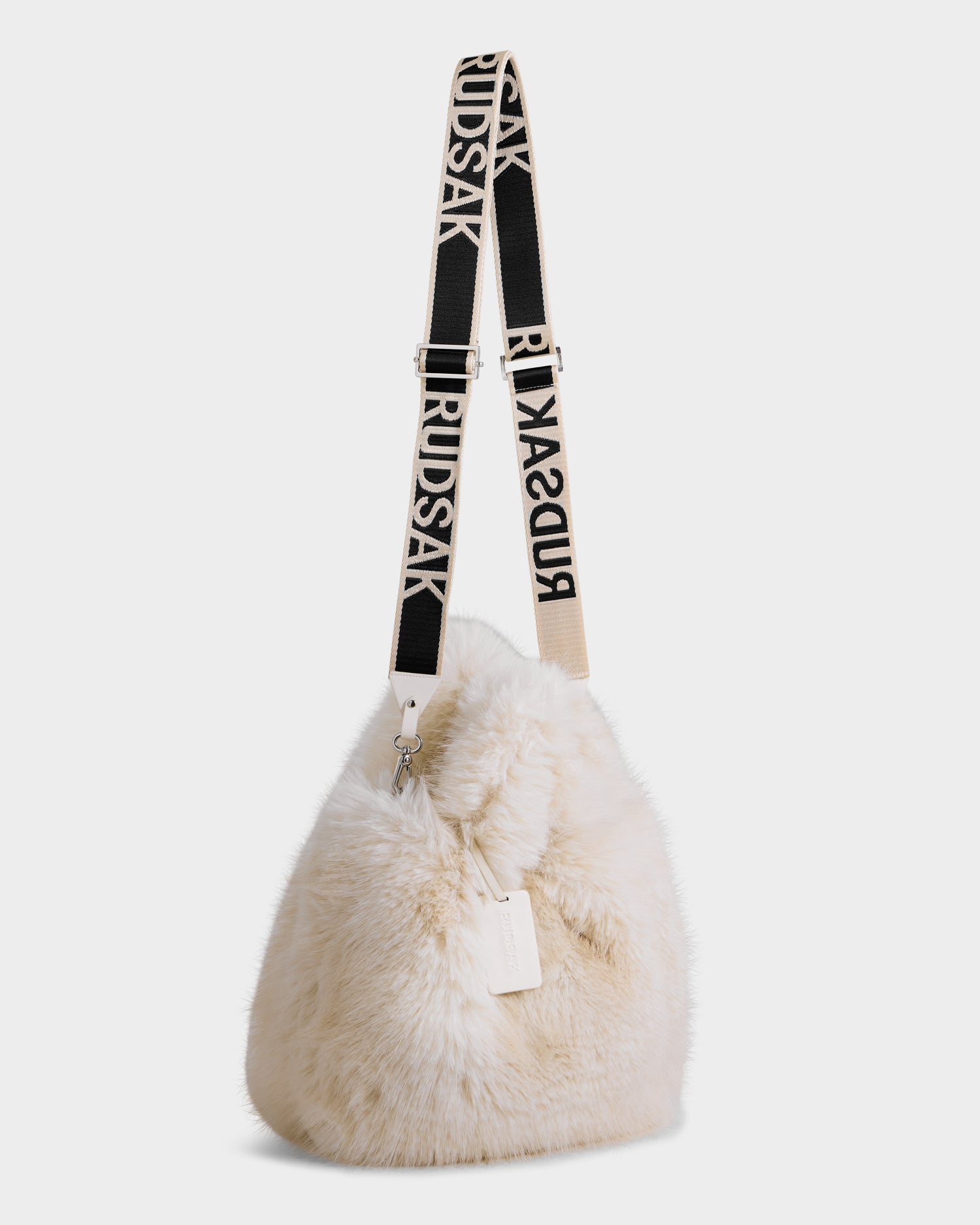 The CABAS - 8325545 Vanilla by Rudsak is a cream-colored, fuzzy faux fur mini tote with a black and white RUDSAK logo strap and a simple tag, pictured against a plain white background.