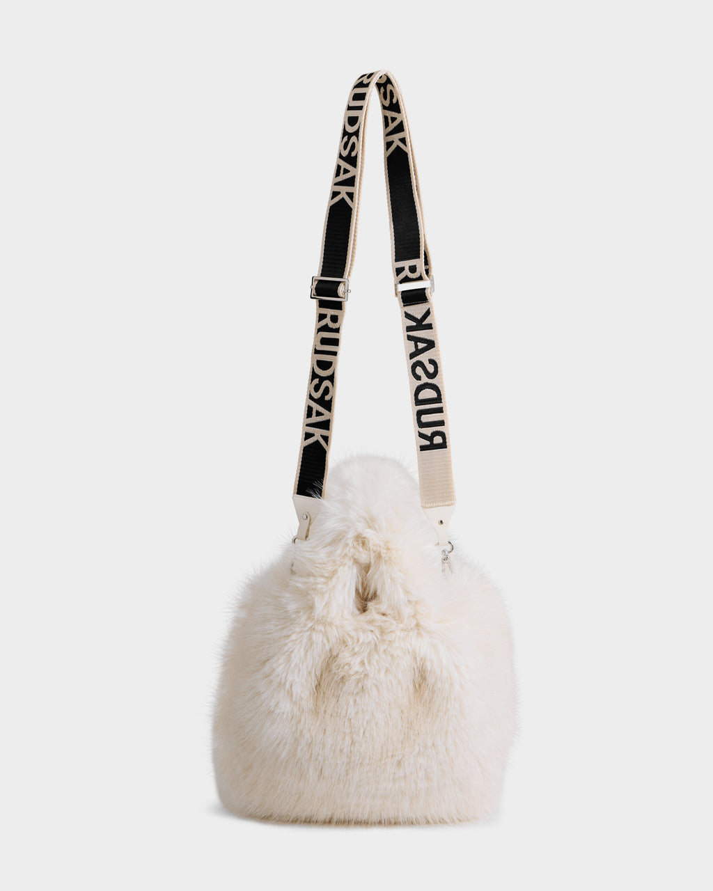 The CABAS - 8325545 Vanilla by Rudsak is a white faux fur mini tote bucket bag with a black and white RUDSAK-branded adjustable strap and a plush texture. Its drawstring closure makes it a standout accessory for winter outfits.