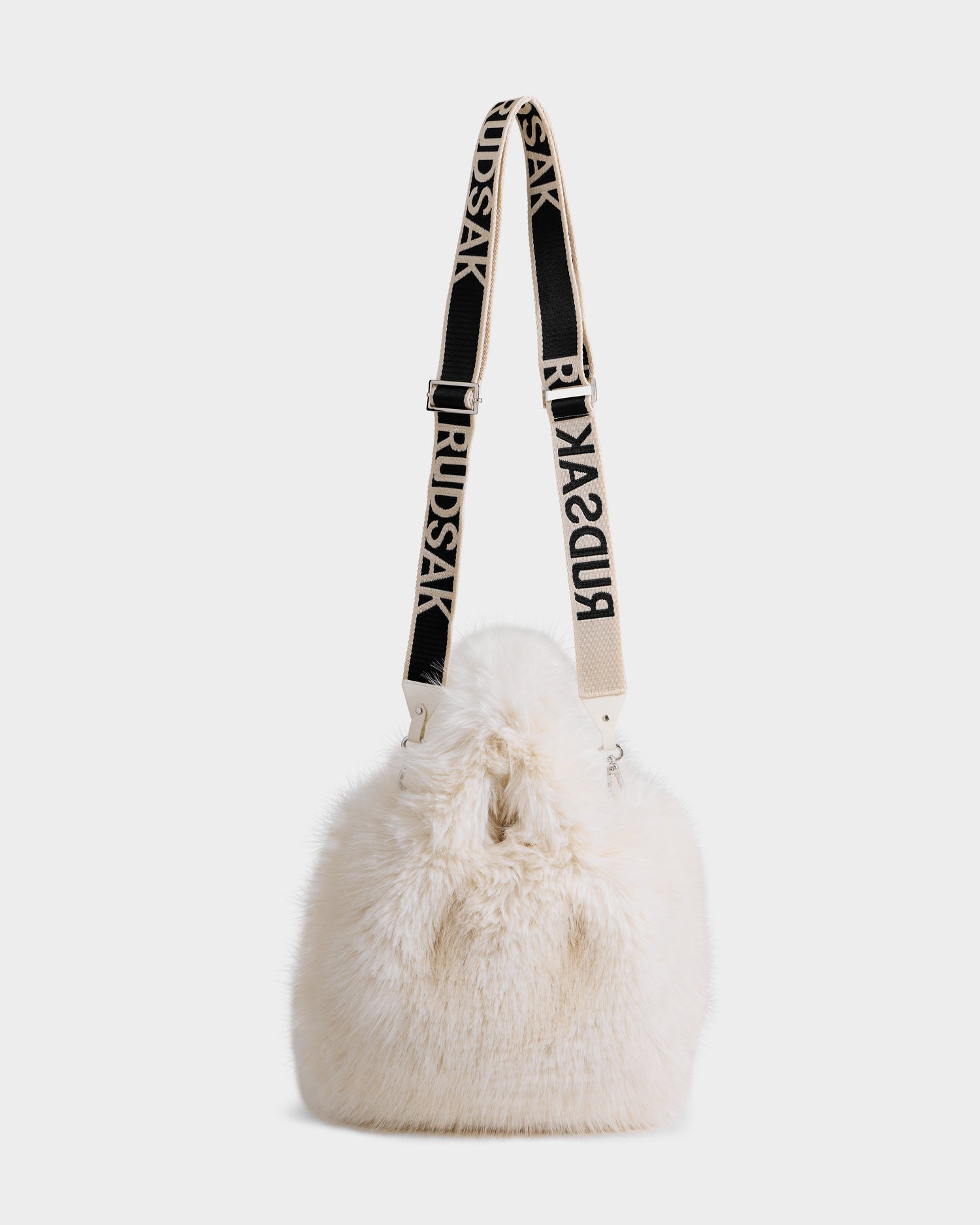The CABAS - 8325545 Vanilla by Rudsak is a white faux fur mini tote bucket bag with a black and white RUDSAK-branded adjustable strap and a plush texture. Its drawstring closure makes it a standout accessory for winter outfits.