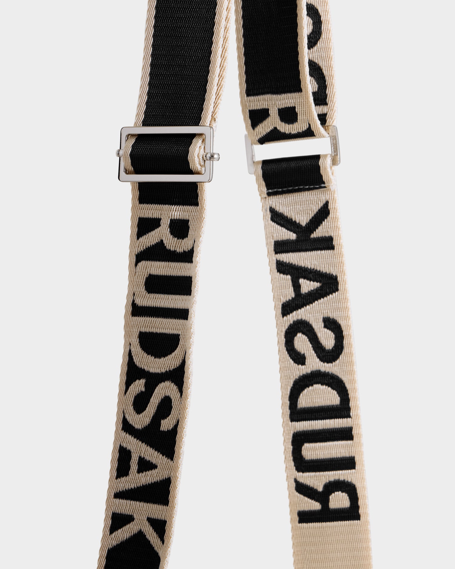 Close-up of two fabric straps, one black and one beige, both featuring "Rudsak" woven into the material. Pair these with the CABAS - 8325545 Vanilla mini tote for a chic statement accessory to elevate your winter look.