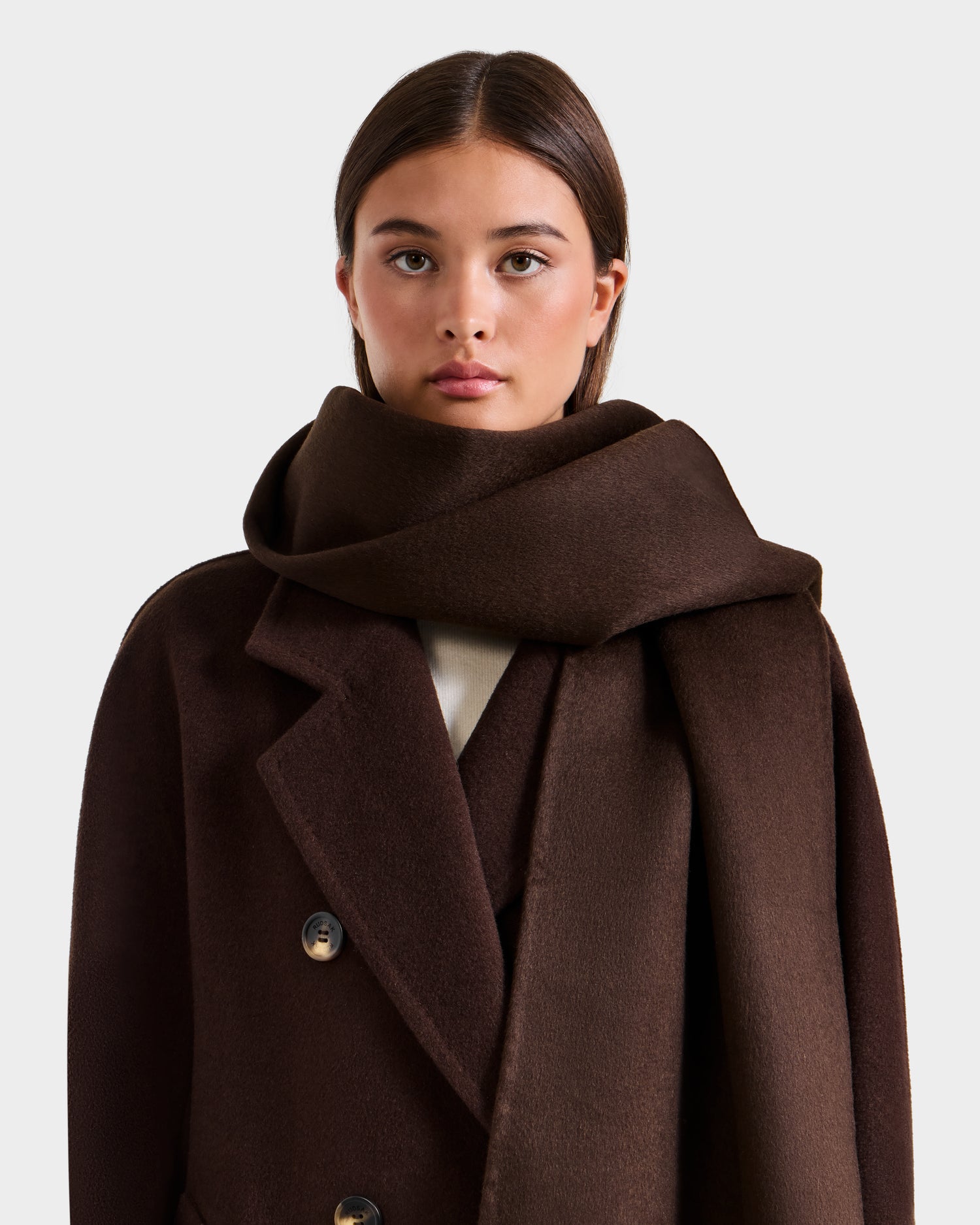 A woman with long brown hair wears the Rudsak CALEN - 8425532 Espresso dark brown coat and a matching wool blend scarf, standing against a light gray background and looking directly at the camera with a neutral expression.