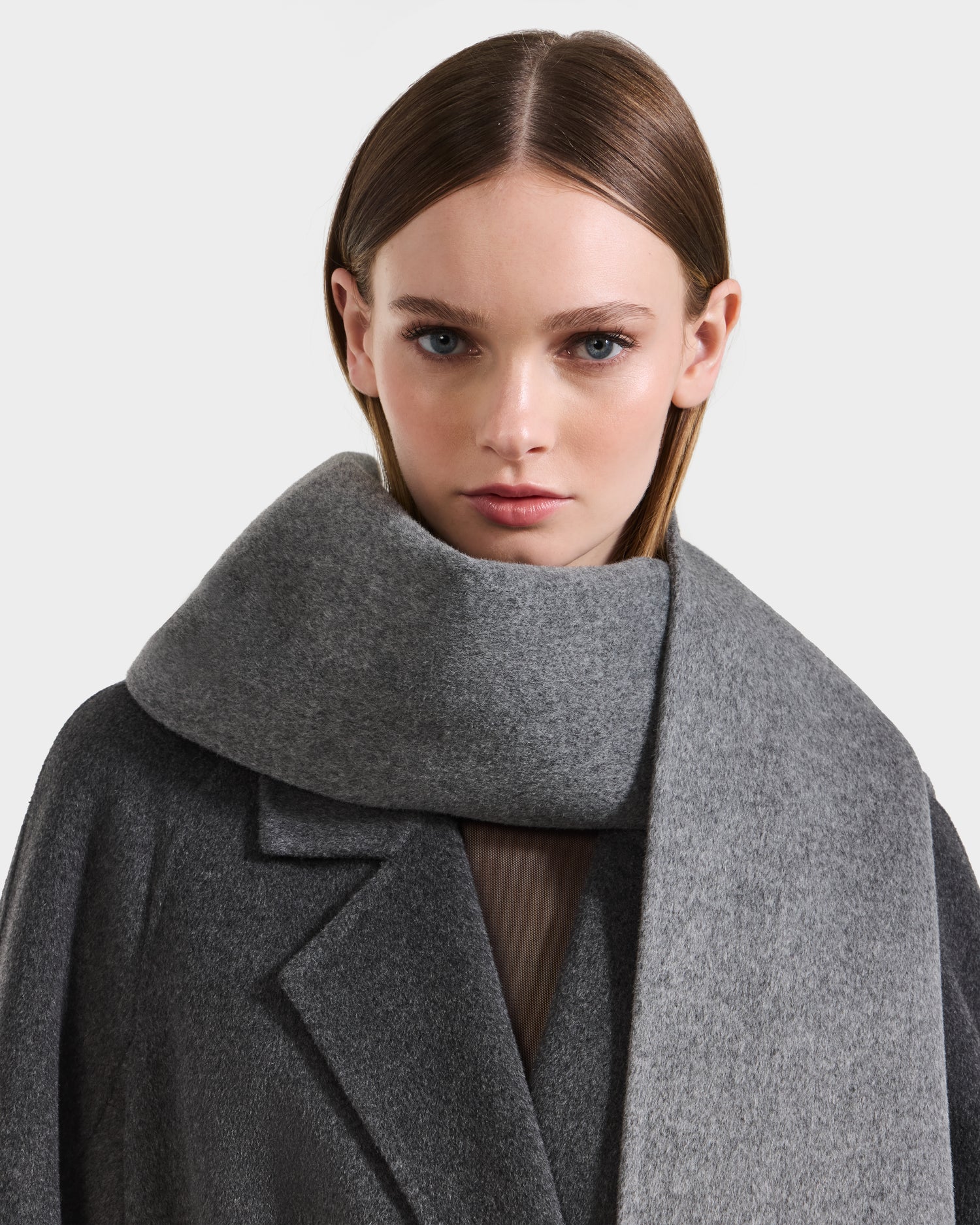 A woman with straight, light brown hair wears the Rudsak CALEN - 8425532 Grey unisex wool scarf around her neck and a dark grey coat, looking directly at the camera against a plain light background.