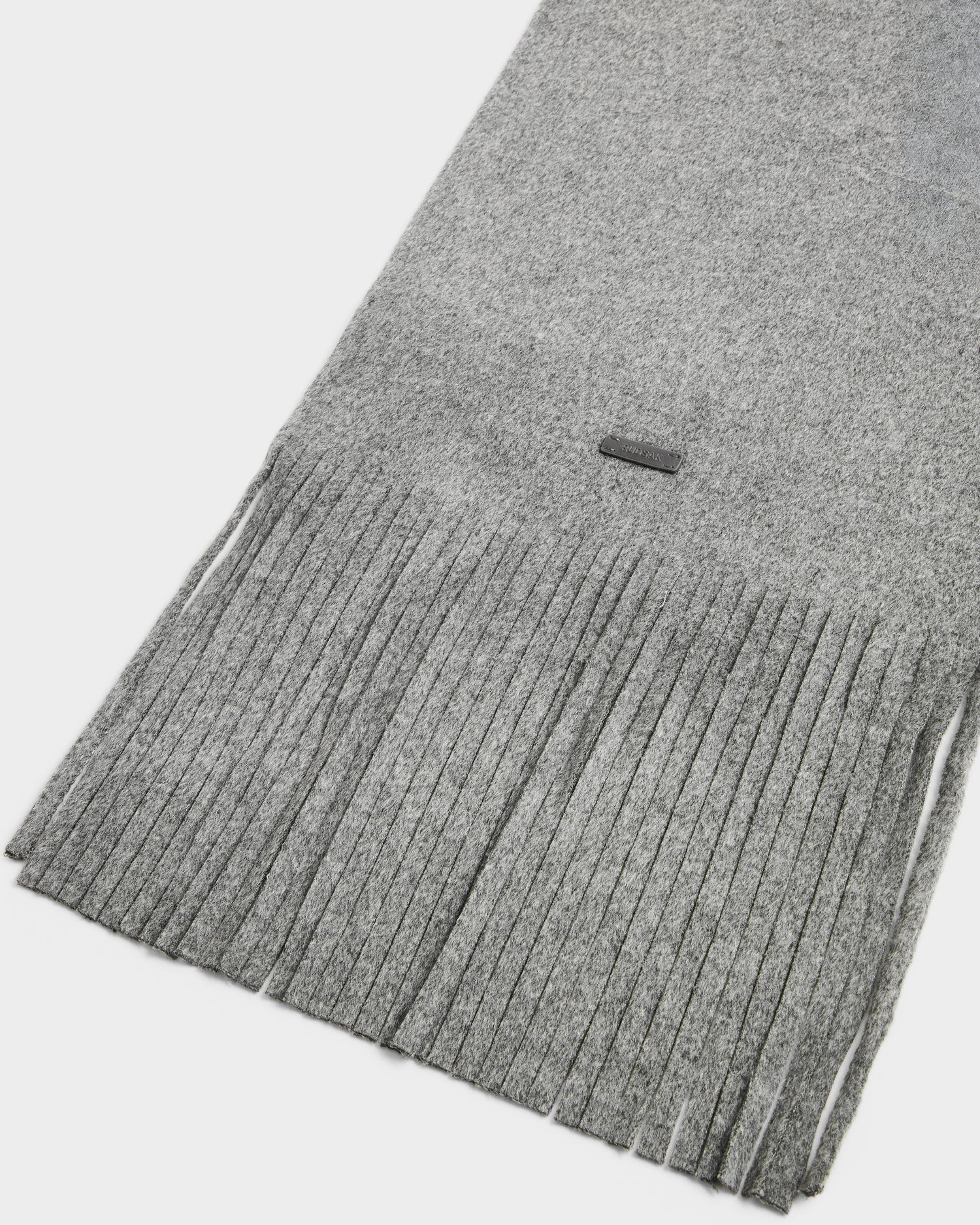 A close-up of the CALEN - 8425532 Grey wool blend scarf by Rudsak, featuring soft light gray fabric, long even fringes, and a small rectangular tag near the edge—making it a stylish cold-weather accessory.