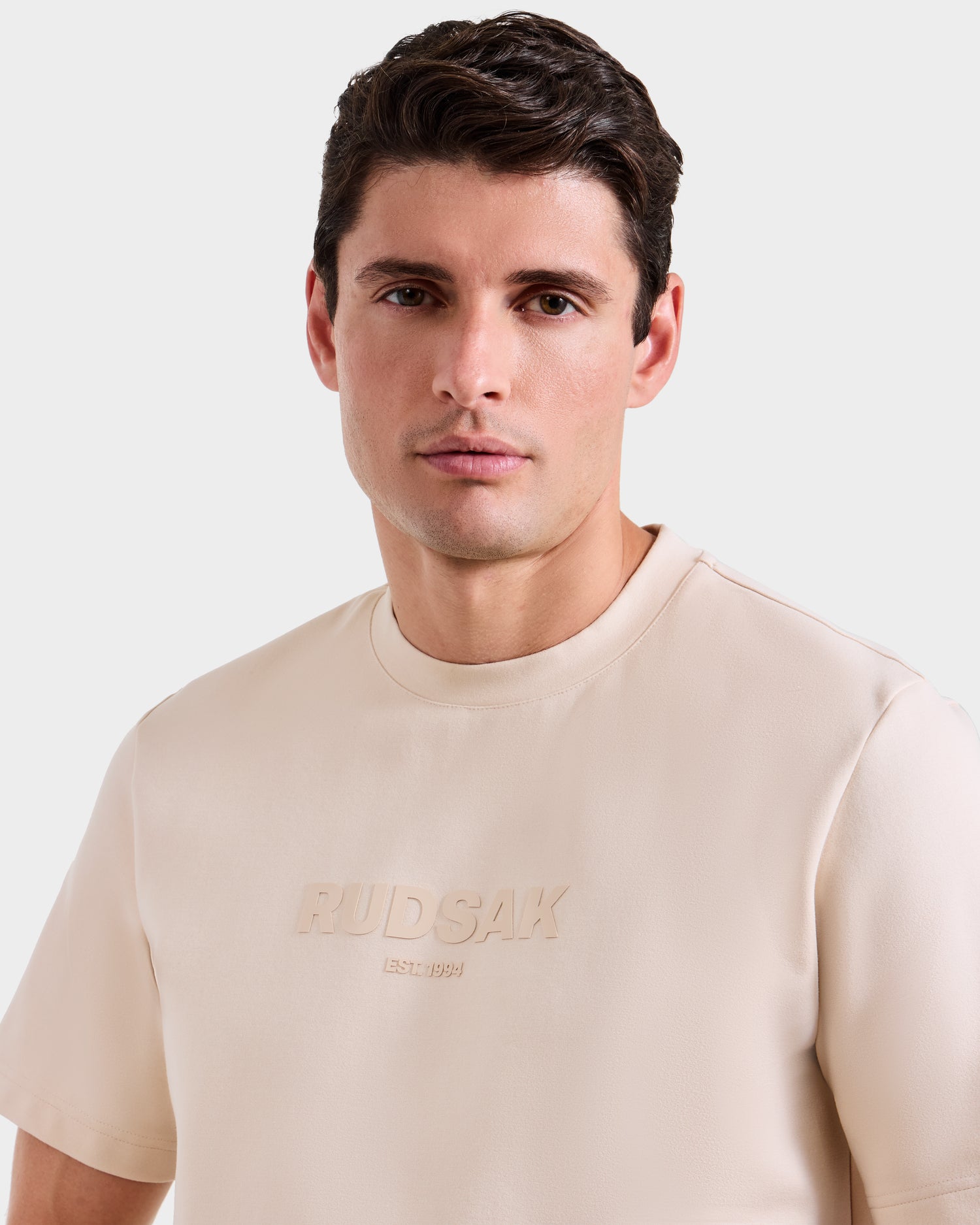 A man with short brown hair models the Rudsak CASEY - 6525037 Vanilla T-shirt, an effortlessly comfortable mens essential, as he looks directly at the camera against a plain light background.