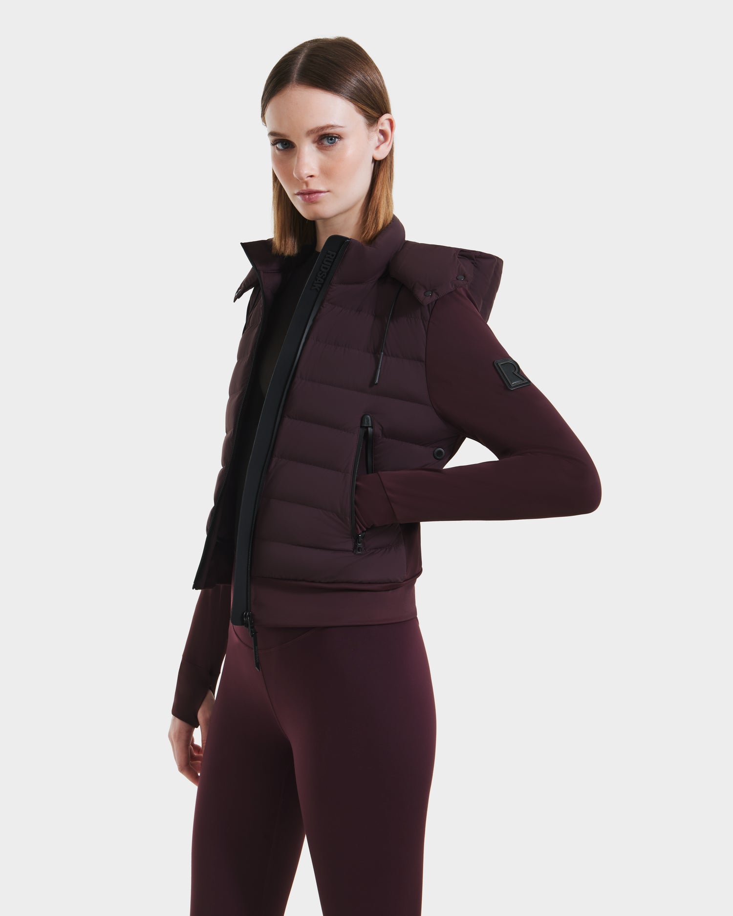 A woman wears the Rudsak CASSA - 8125057 Bordeaux lightweight cropped jacket over a matching fitted top and pants, standing confidently against a white background.