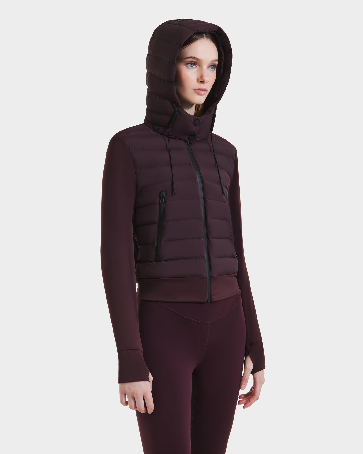 A woman stands facing forward against a plain white background, wearing the Rudsak CASSA - 8125057 Bordeaux transitional jacket with zippered pockets and matching fitted leggings.
