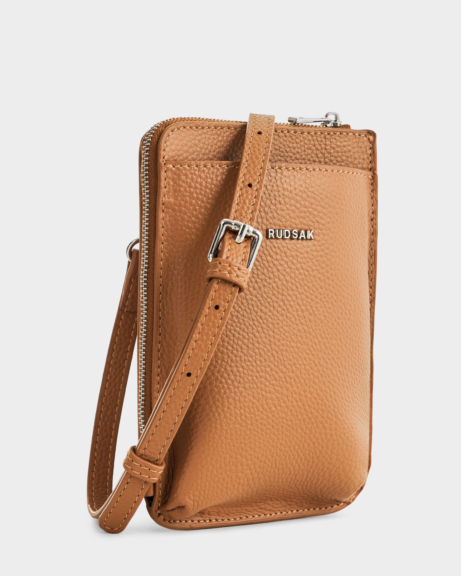The Rudsak CELYN - L325514 Taupe is a small women’s city bag in tan pebbled leather, featuring an adjustable strap with a silver buckle, RUDSAK’s silver logo on the front, and a top zipper closure for security.