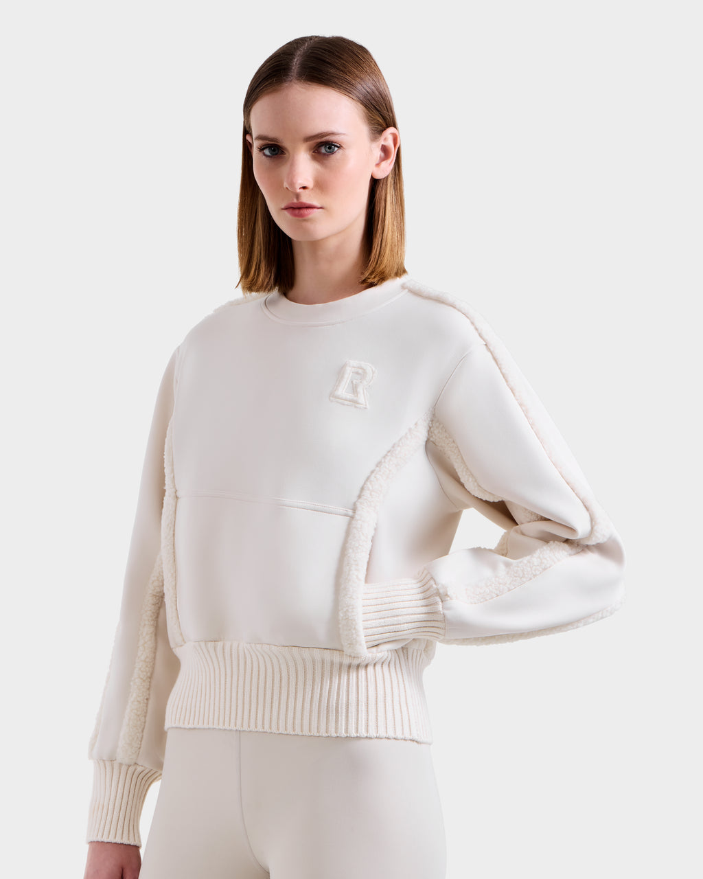 A woman models the Rudsak CHANA - 8525656 Vanilla women’s crew neck sweatshirt, featuring textured faux shearling and an embossed “R” on the chest, paired with matching pants against a simple light background.