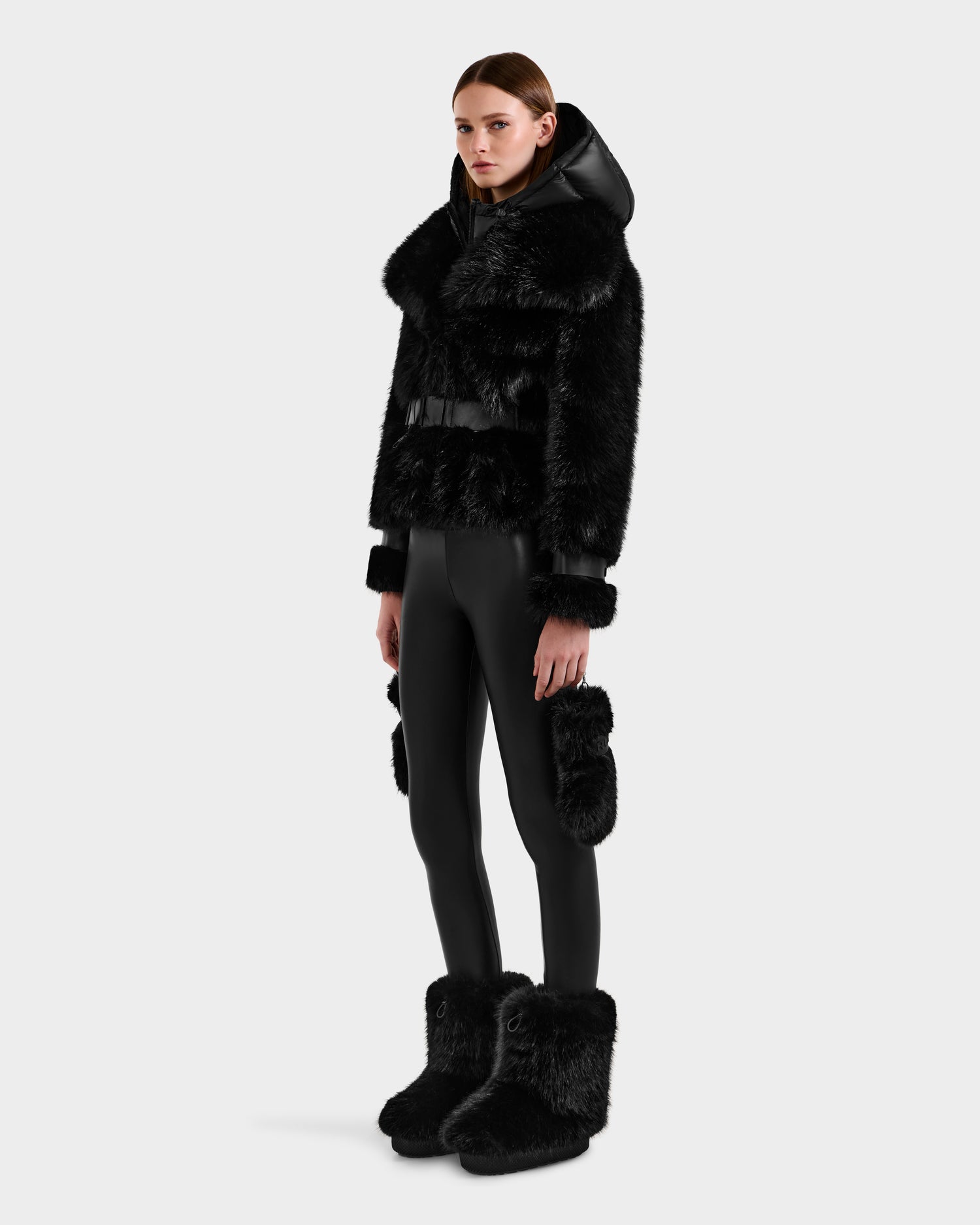 A woman faces forward against a white background, modeling the Rudsak CHLOE - 8125619 Black women's faux fur jacket with matching fur-trimmed leggings and large fur boots. Her hair is straight and parted in the middle.