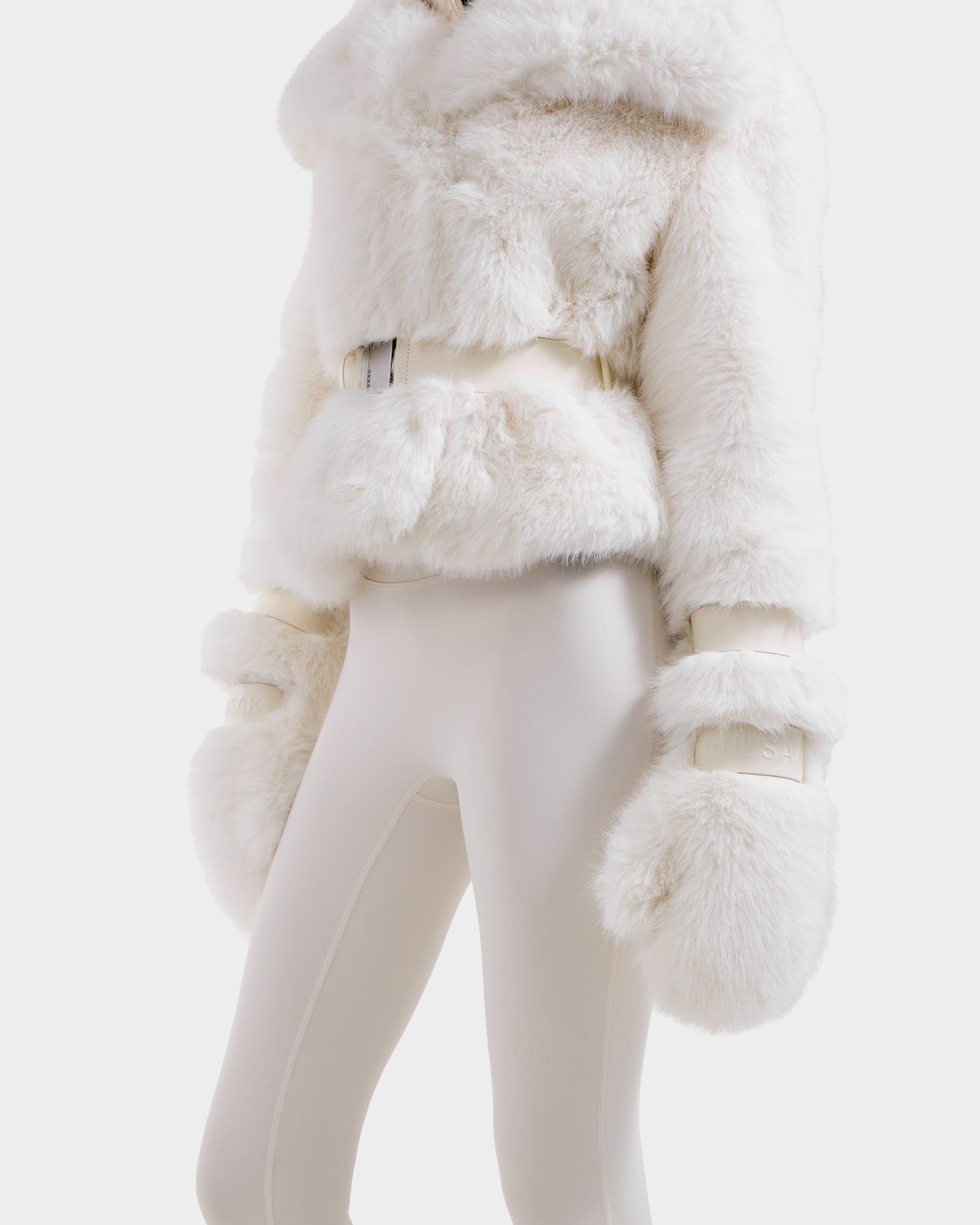 A model wears the Rudsak CHLOE - 8125619 Iceland women's faux fur jacket with a belt, white mittens, and fitted pants, embodying chic winter style, shown shoulders down on a plain white background.
