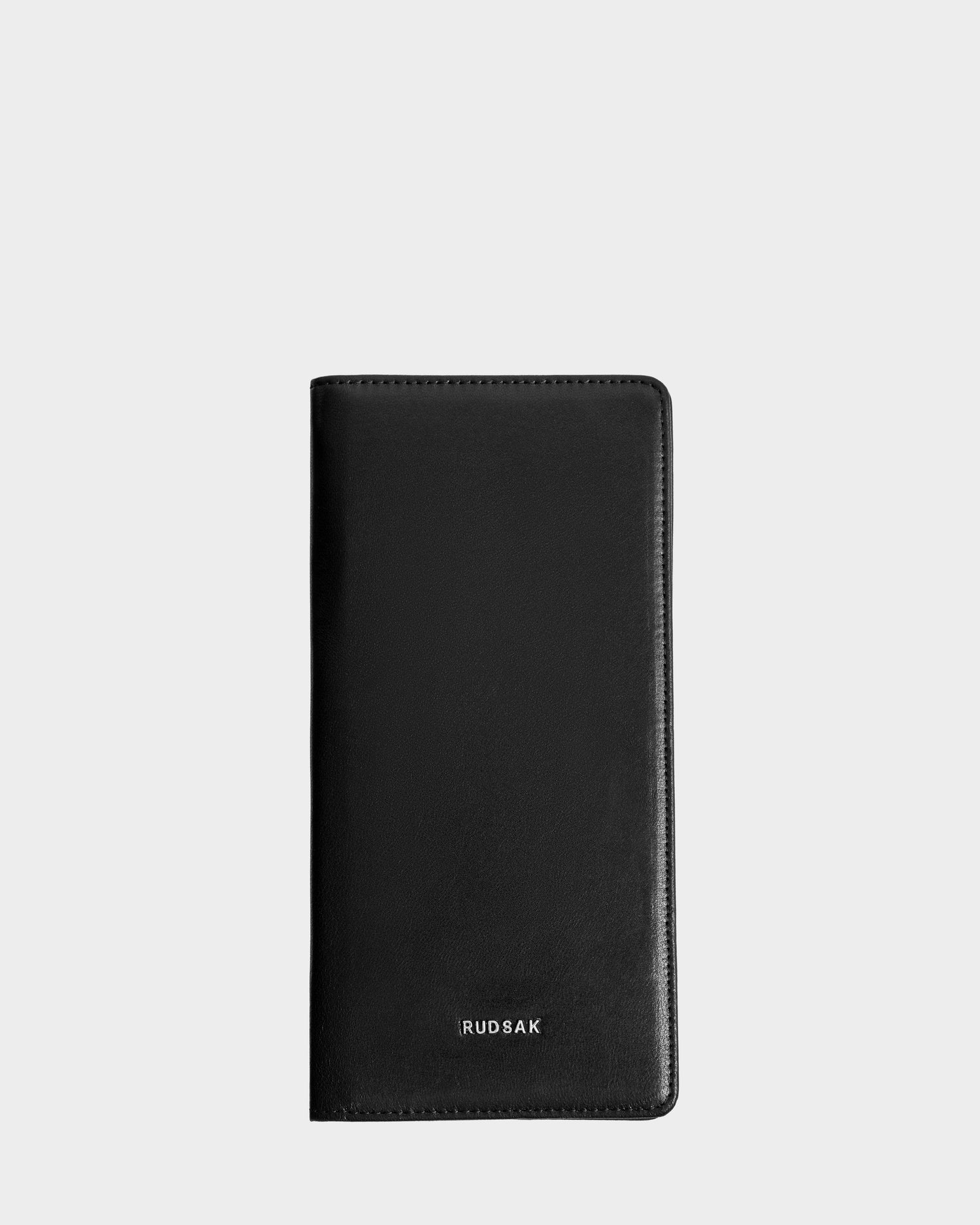 The CLEO - 9425522 Black passport holder by Rudsak features black leather and silver embossed branding near the bottom center, displayed upright against a plain light gray background—an elegant accessory for any journey.