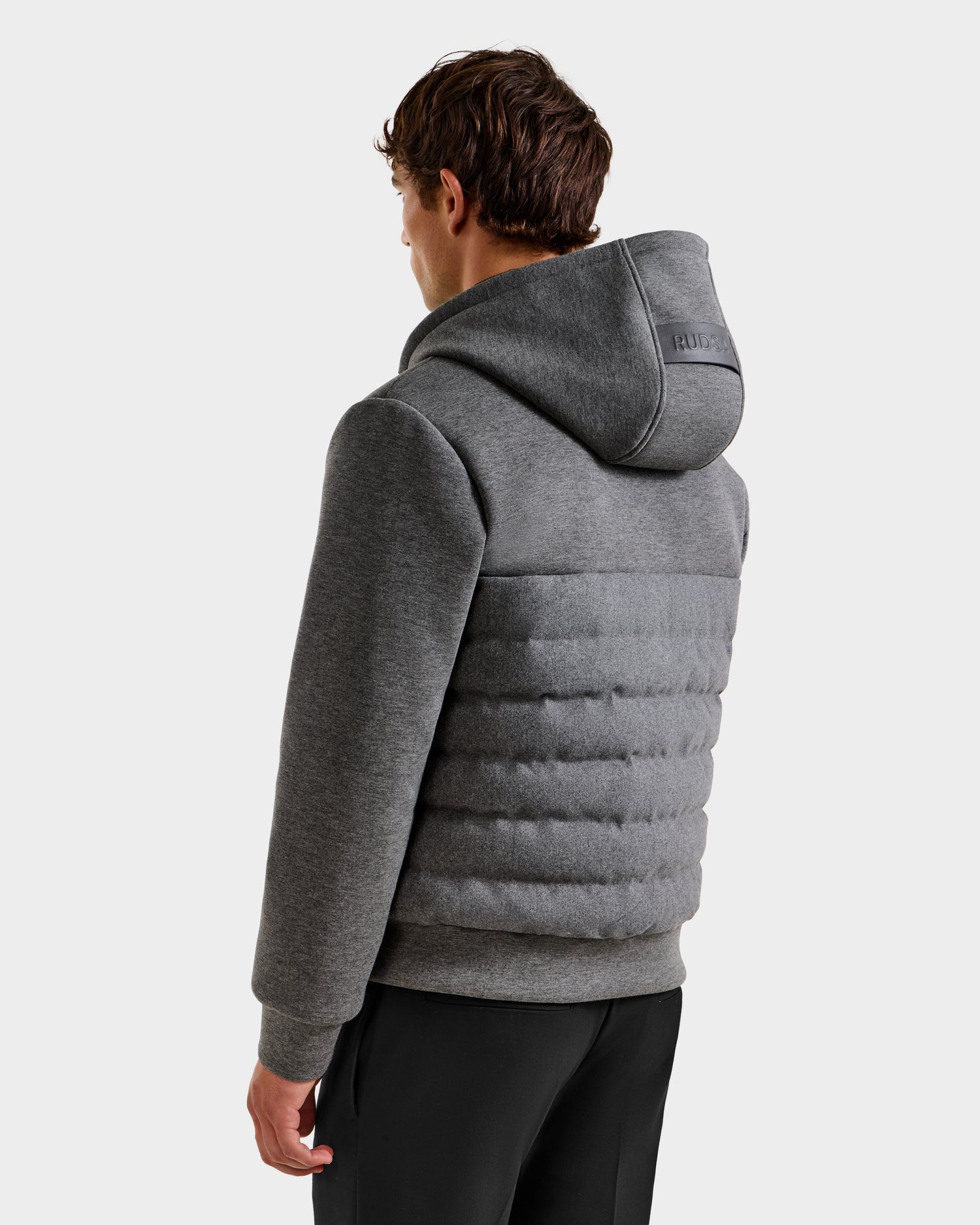 A man is shown from the back, wearing the Rudsak CURTIS W - 6125581 grey men’s lightweight down jacket with a quilted design and black pants, standing against a plain white background.