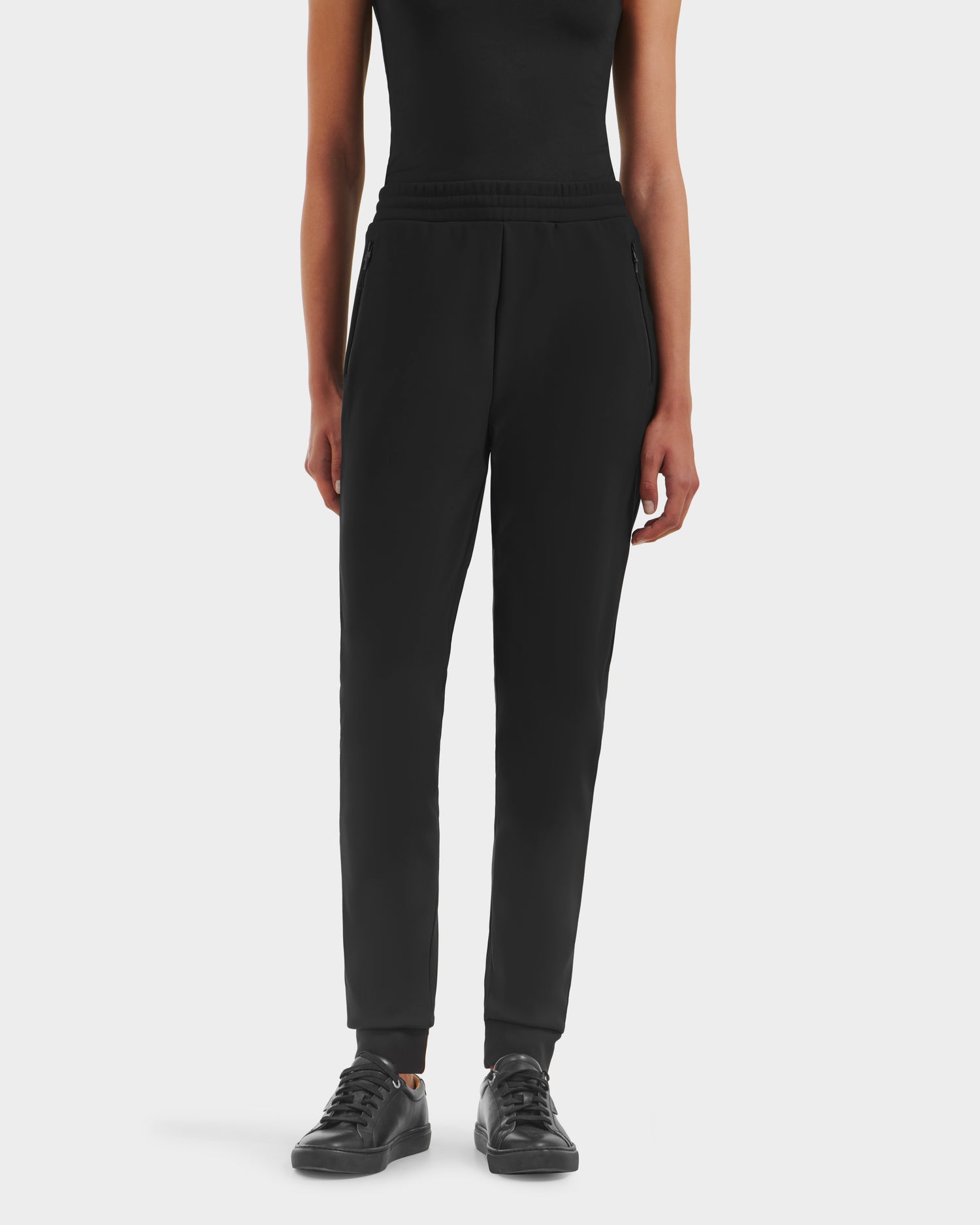 A person showcases athleisure style wearing the Rudsak DAMERIS - 8525575 Black jogger pants with a black sleeveless top and sneakers, set against a plain white background. The image is cropped from the shoulders down.