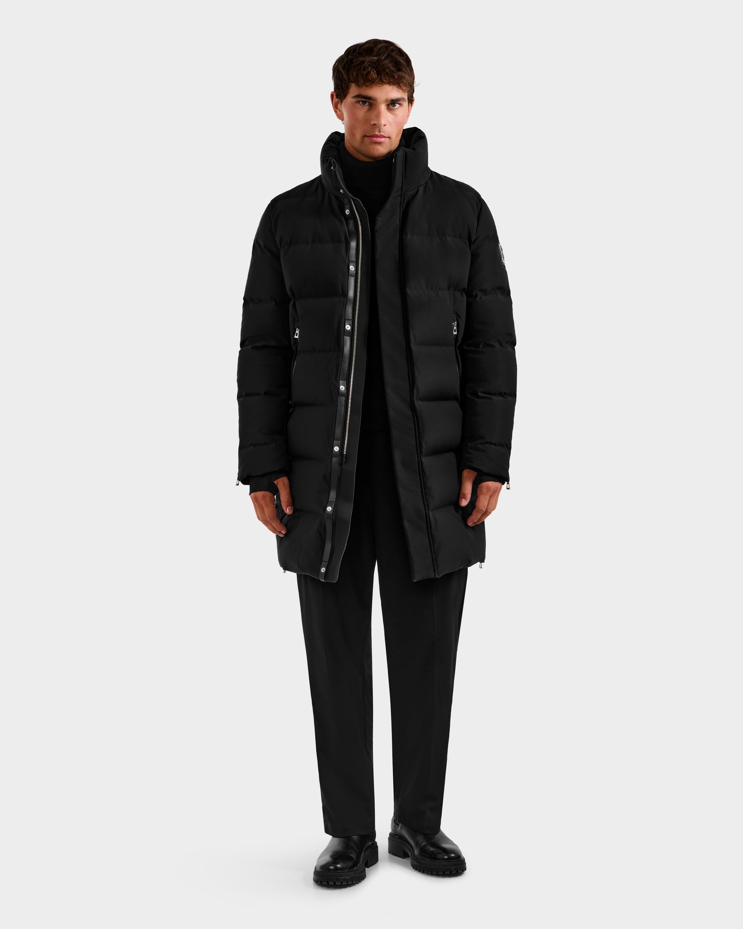 A man faces forward, wearing the Rudsak DAO H - 6125583 Black quilted down jacket as winter outerwear over a black turtleneck, pants, and shoes, set against a plain light gray background.
