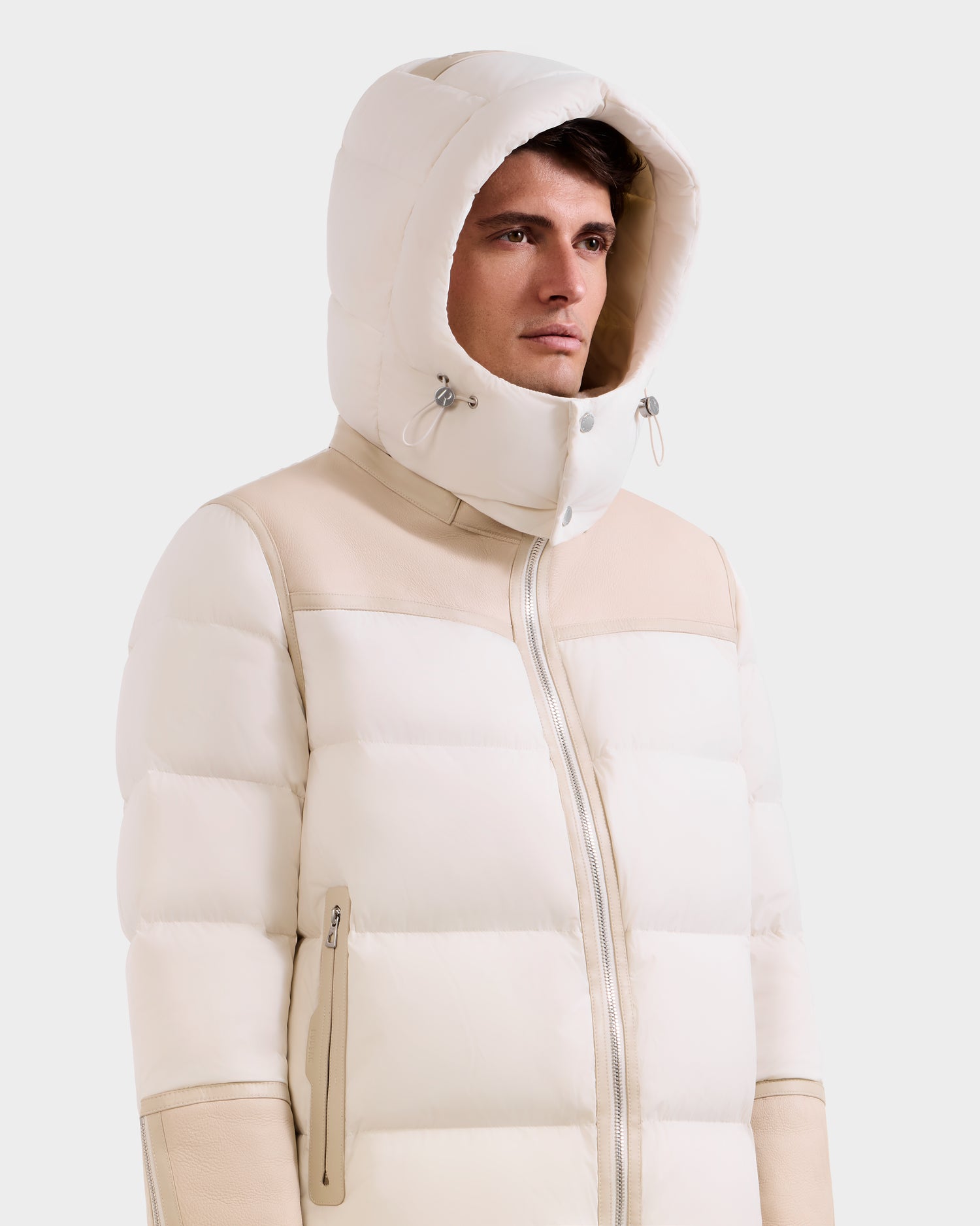 A person models Rudsak's DAVID - M125508 Vanilla: a white padded jacket with hood, beige accents, high collar, and zippered pockets—combining cozy warmth and practical style against a plain light background.