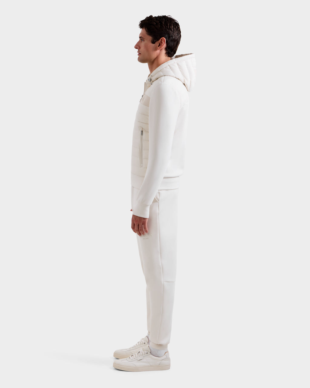 A man stands in profile wearing Rudsak’s DEE MP - 6125673 Vanilla, a men’s lightweight down jacket with RDS-certified duck down, paired with matching pants and white sneakers against a plain white background—a perfect transitional staple.