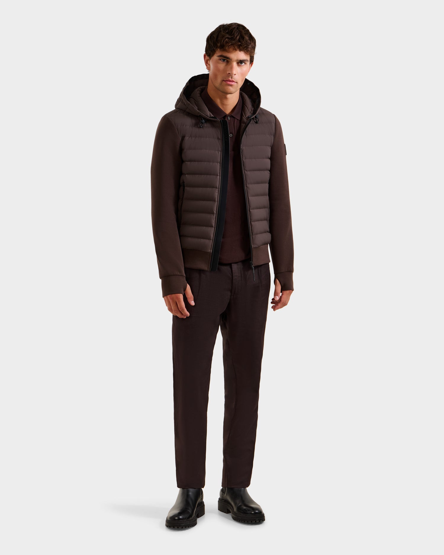 A young man faces forward, wearing the Rudsak DEE MAT - 6124028 Espresso men's lightweight hybrid down jacket, paired with dark brown pants, a matching shirt, and black shoes against a plain white background.