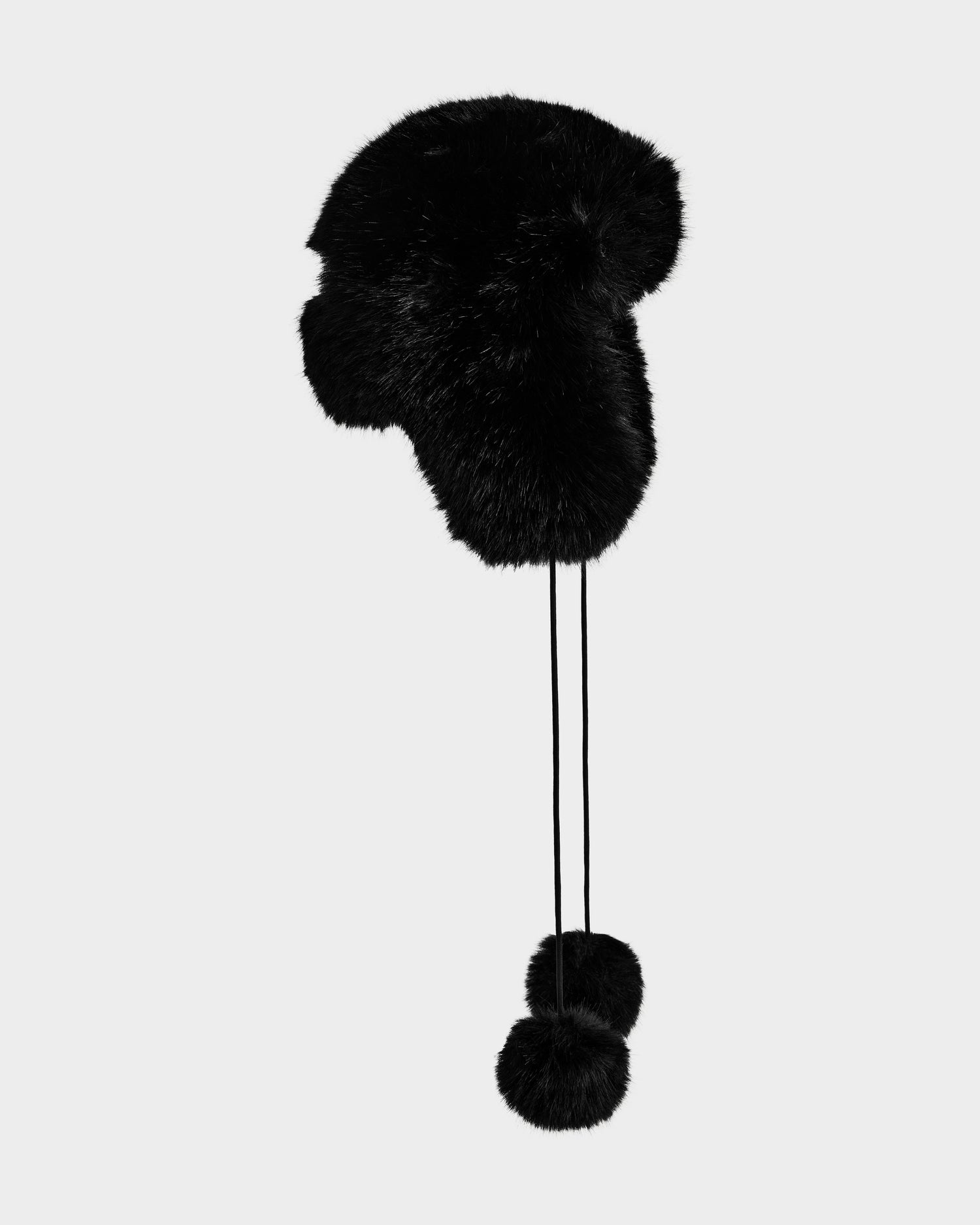A Rudsak DEMI - L425539 black faux-fur aviator hat with ear flaps and two pom-poms on long strings is displayed on a light gray background.