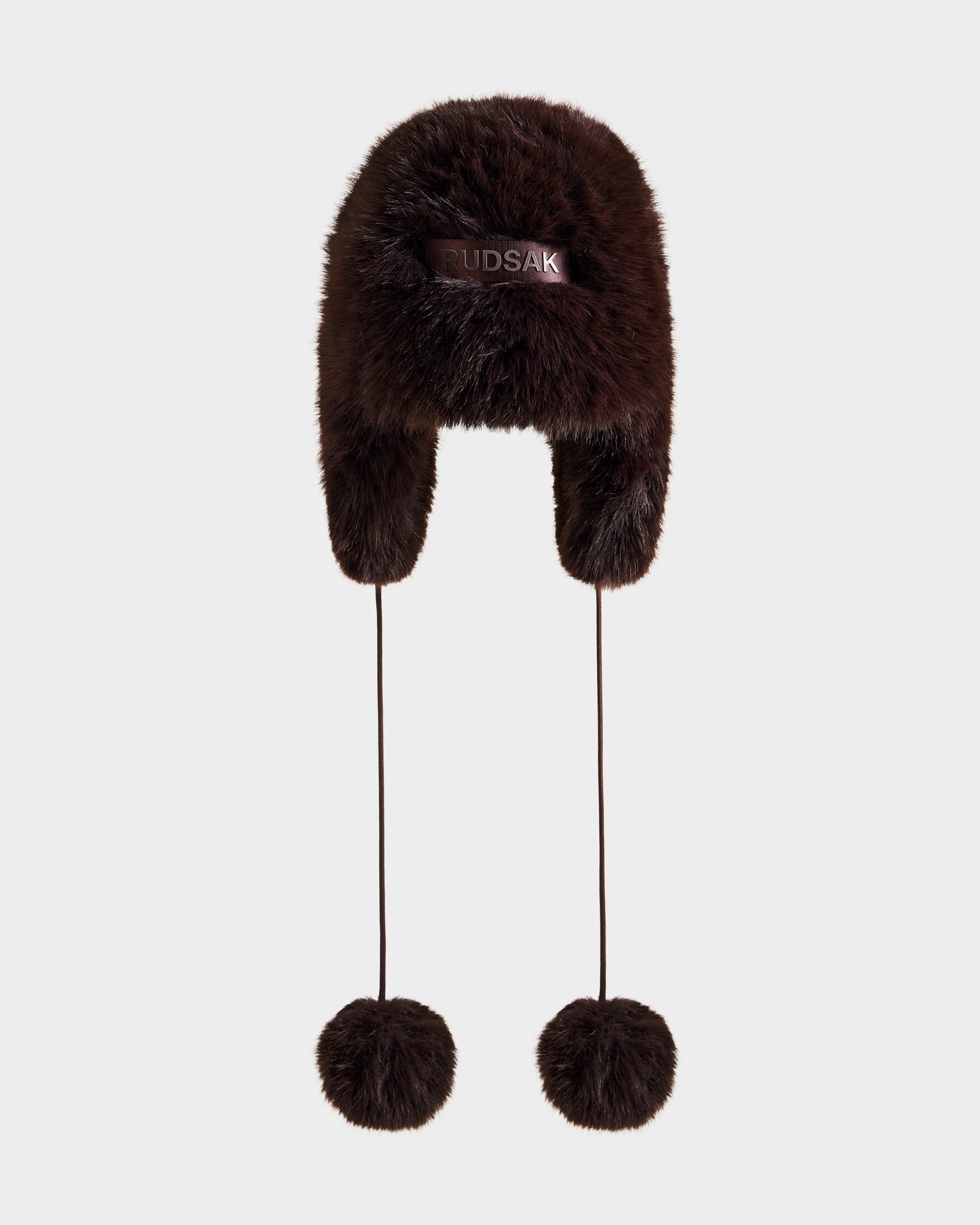 The DEMI - L425539 Espresso by Rudsak is a brown women’s faux-fur aviator hat with ear flaps, long strings with furry pom-poms, and a logo on the front, shown on a plain white background—ideal for winter.