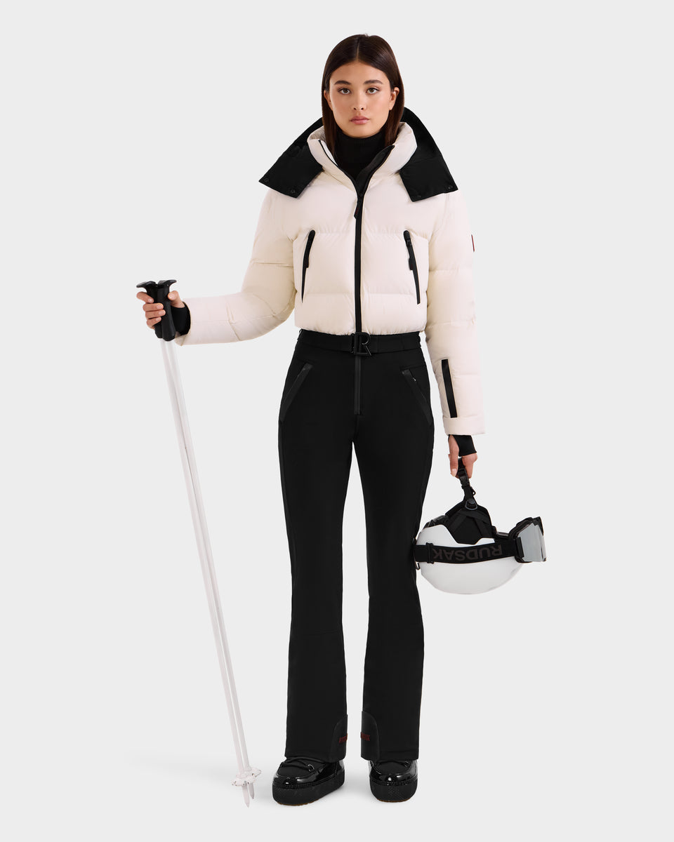 A woman models the Rudsak DINARA - 8125600 Vanilla puffer jacket, holding a ski pole and white helmet, displaying chic après-ski style against a plain white background.