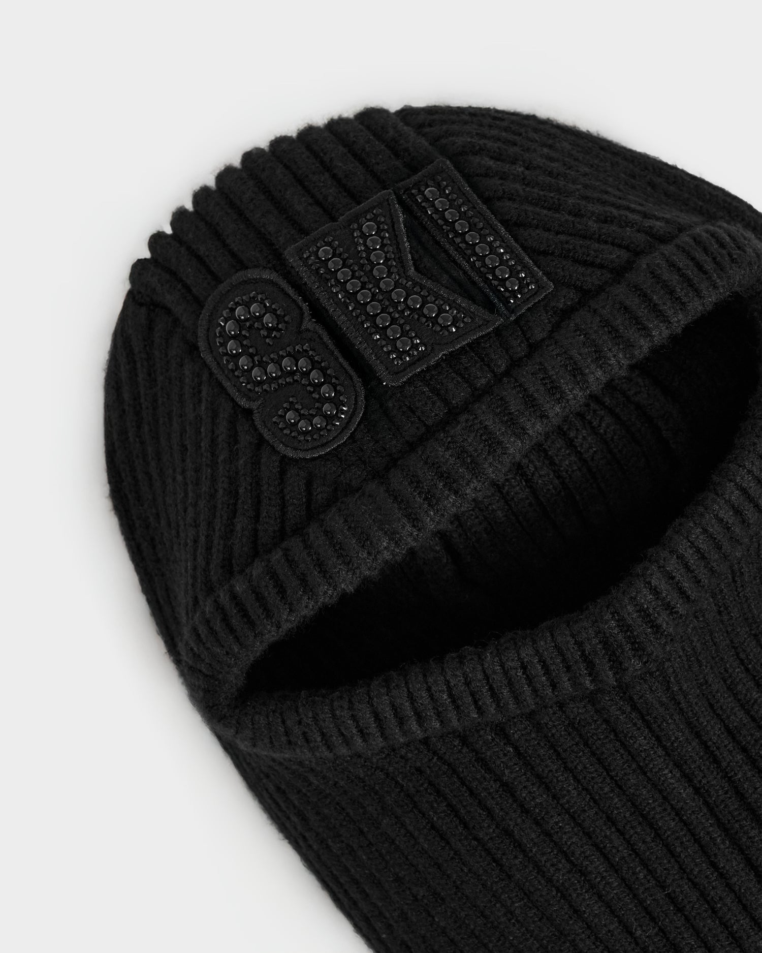 The Rudsak DIXIE - 8425551 Black is a women’s ribbed knit balaclava with a face cutout and a crystal-embellished SKI logo patch—an essential winter accessory.