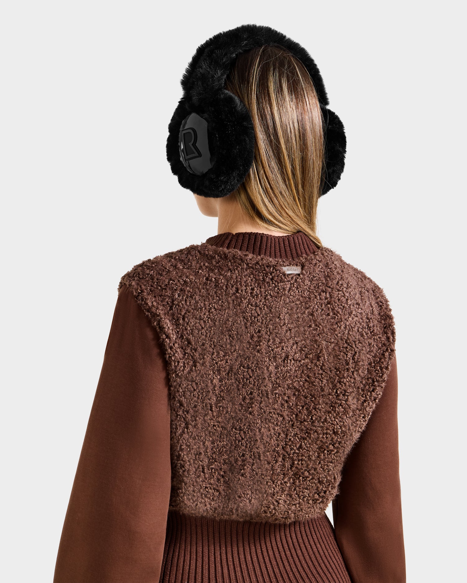 A person is seen from the back in Rudsaks FLORENCE - 8525546 Mocha womens top and black faux fur earmuffs, set against a light background—an après-ski essential blending winter warmth and style.