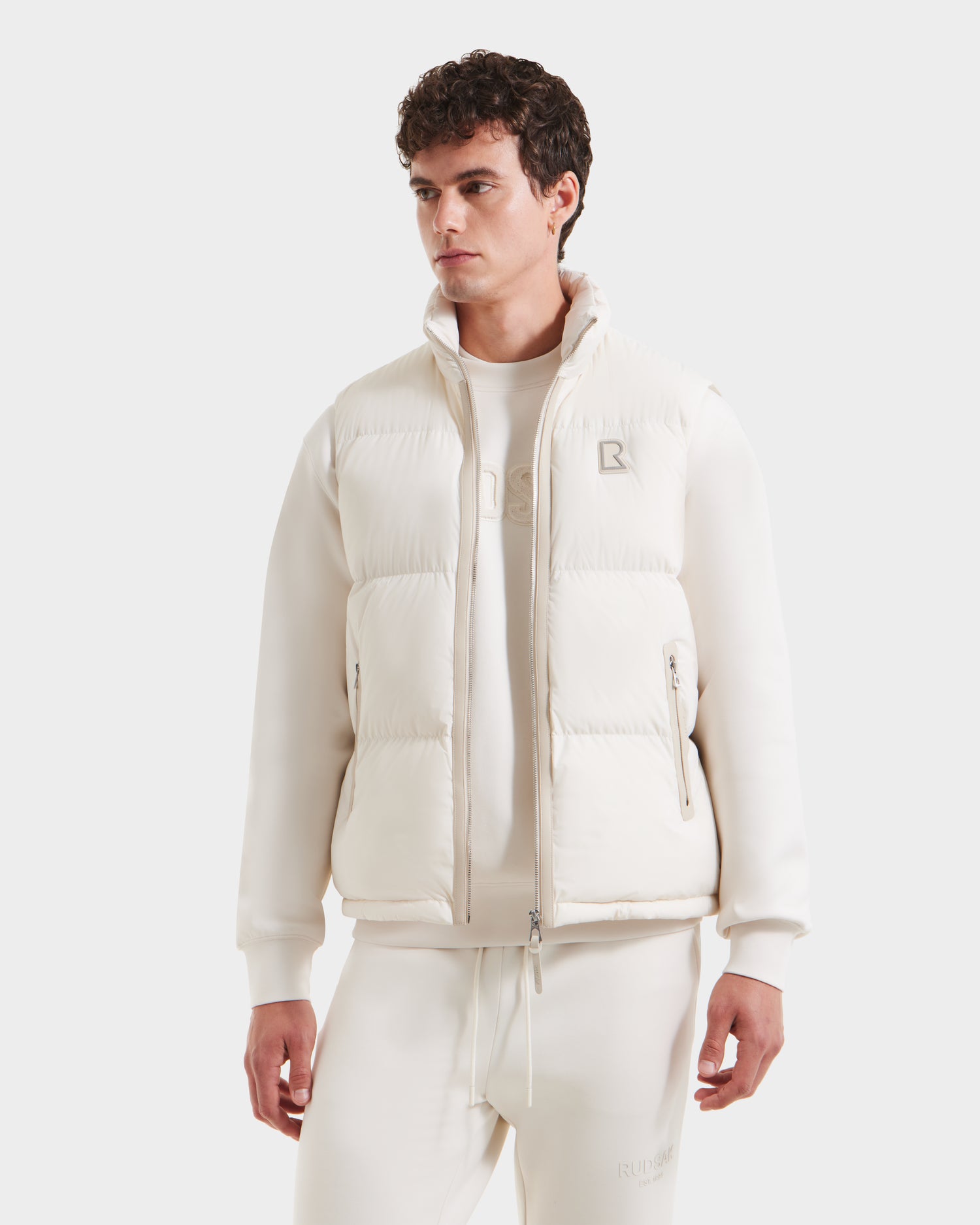 A man in a white jacket styles it with the Rudsak FREDDY - 6125571 Vanilla puffer vest, highlighting lightweight layering and modern appeal.