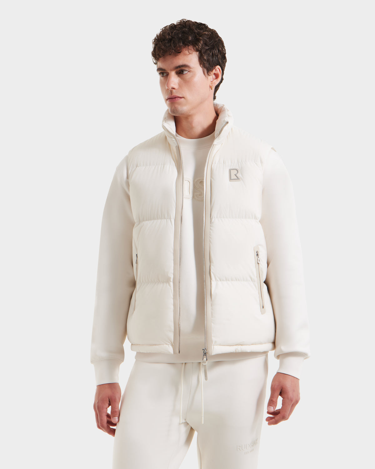 A man in a white jacket styles it with the Rudsak FREDDY - 6125571 Vanilla puffer vest, highlighting lightweight layering and modern appeal.