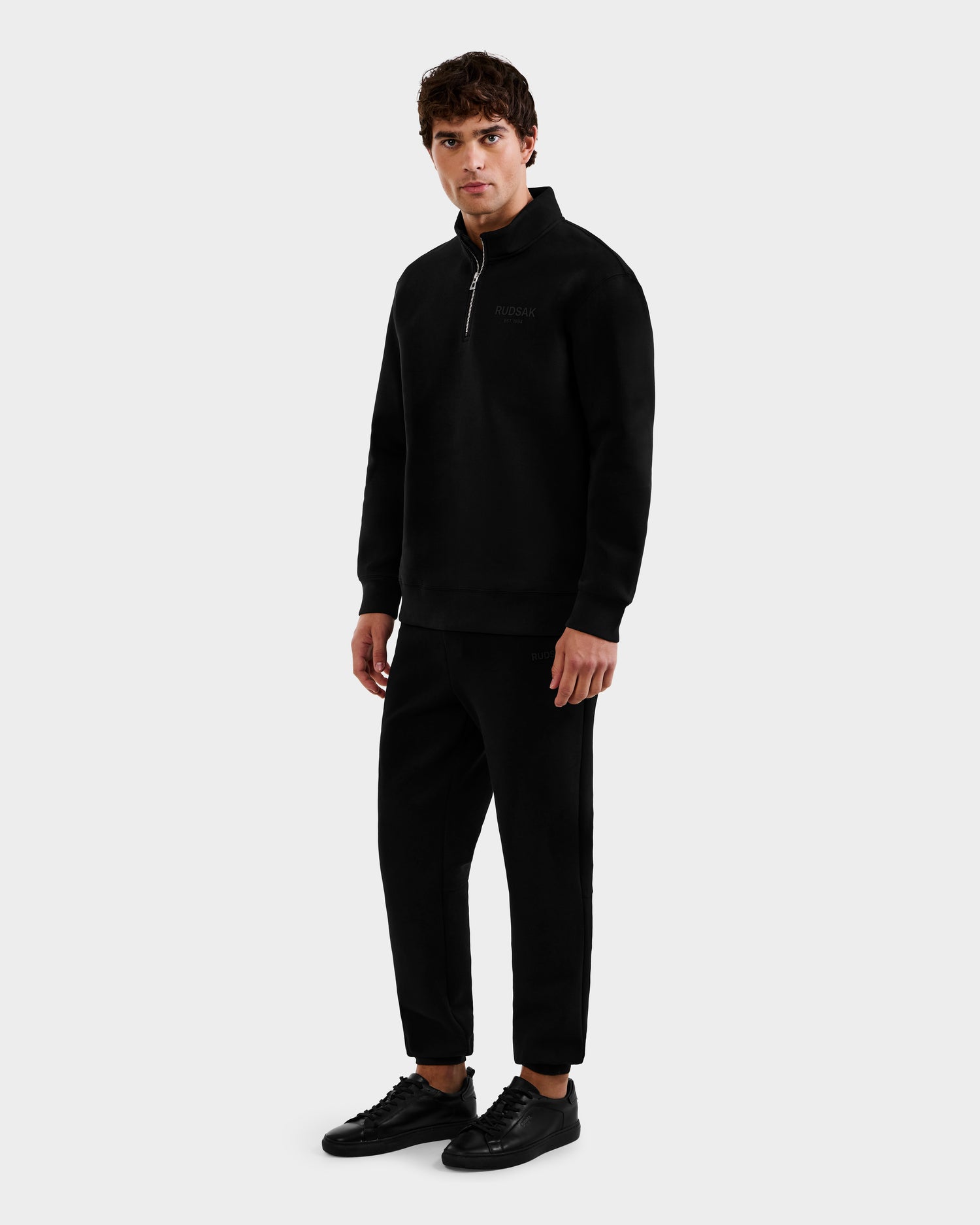 A man faces forward wearing the Rudsak FREMONT - 9525000 Black M, paired with black pants and sneakers, set against a plain light gray background.