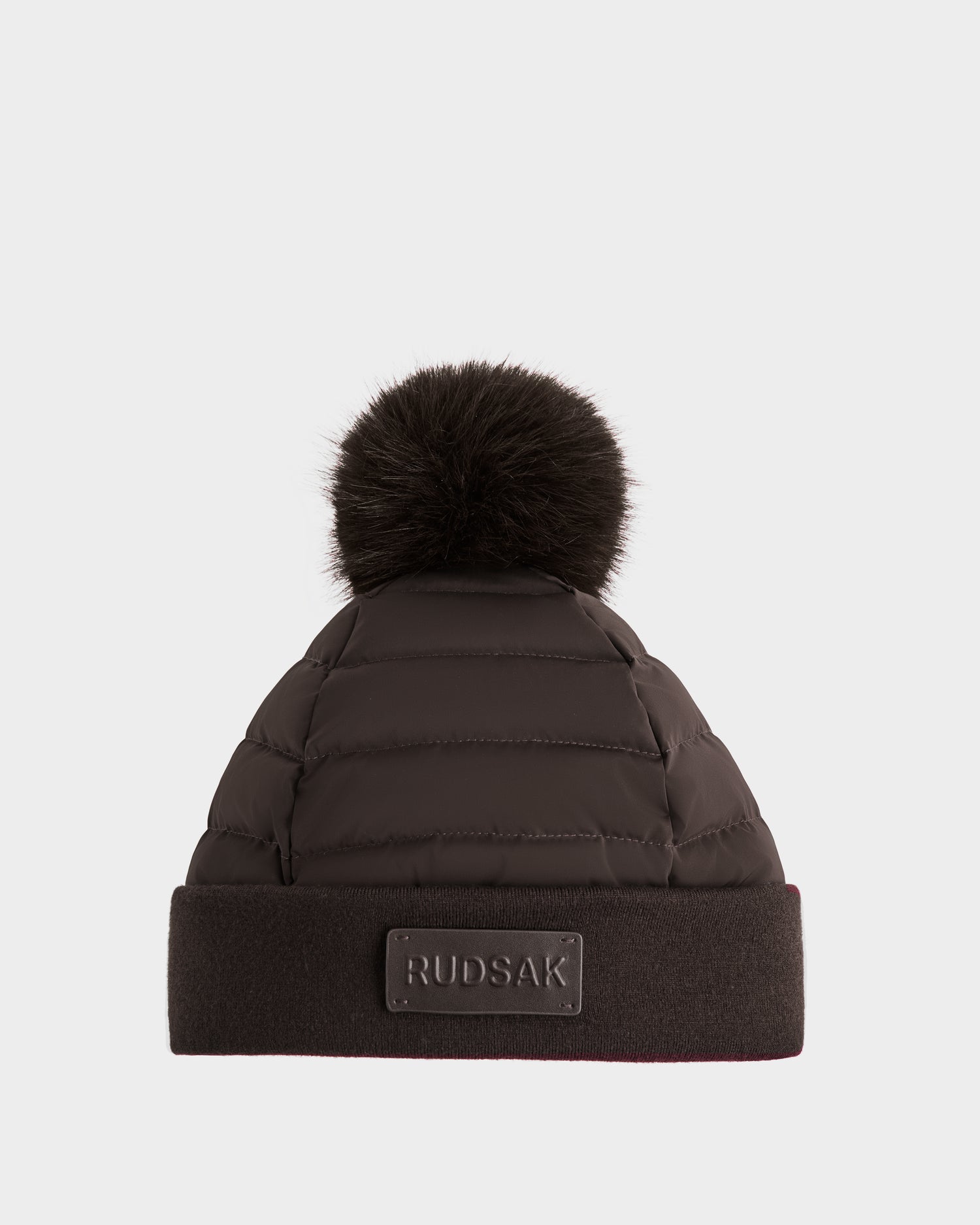 The GALA - 8424514 Espresso by Rudsak is a women's quilted down puffer winter hat in black, featuring a wide brim with Rudsak logo patch and topped with a large faux fur pom-pom.