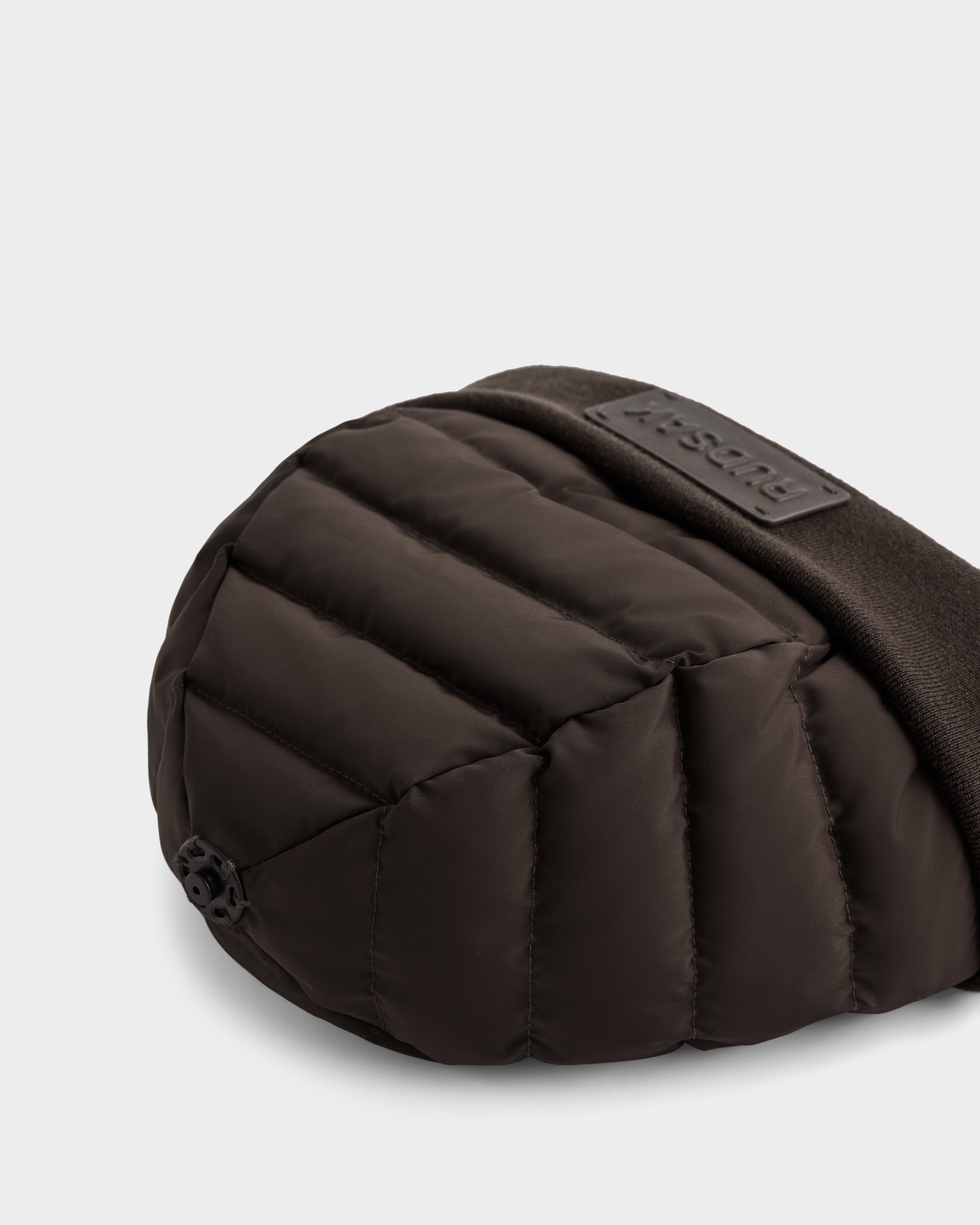 Close-up of the GALA - 8424514 Espresso by Rudsak, a black padded quilted shoulder or waist bag with a fabric strap and small black logo tag, set against a light gray background—perfect to pair with your favorite winter hat.
