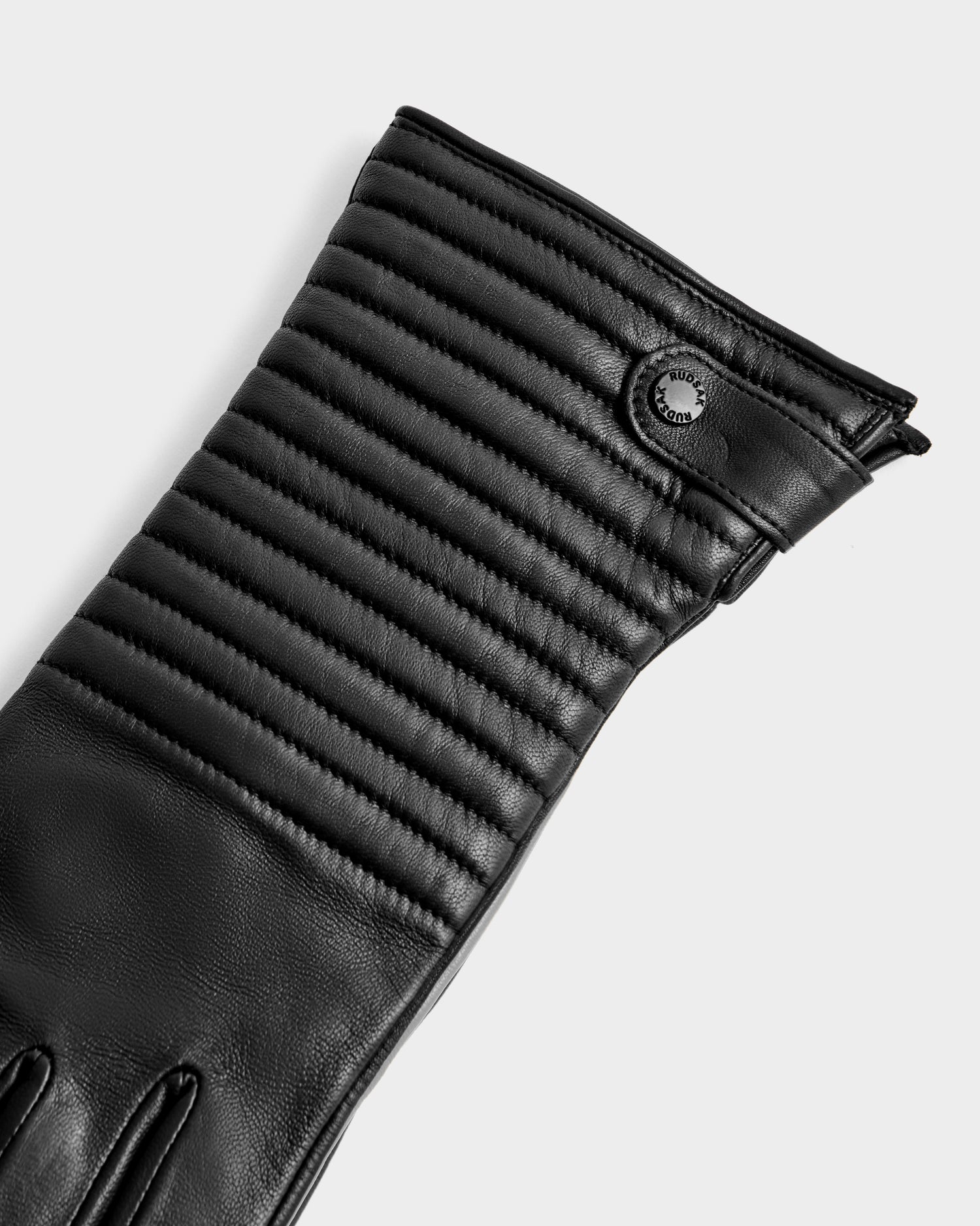 A close-up of the Rudsak GEMMA - 8425008 Black glove showcases its quilted stitching and round black cuff button, set against a light background—an elegant winter accessory ideal for chilly days.