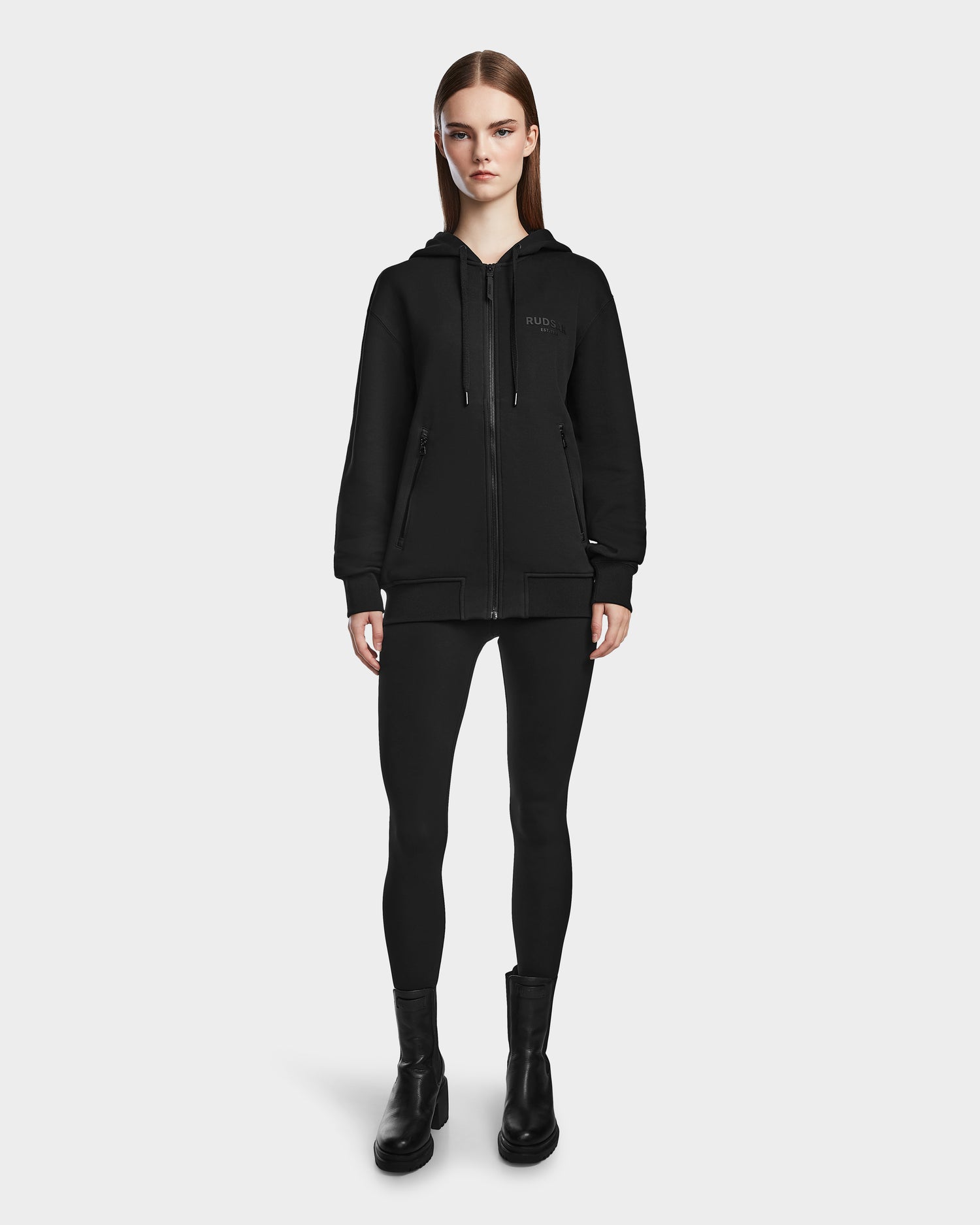 A woman faces forward against a white background, wearing the JACE - 9524010 Black W hoodie by Rudsak, paired with black leggings and boots.