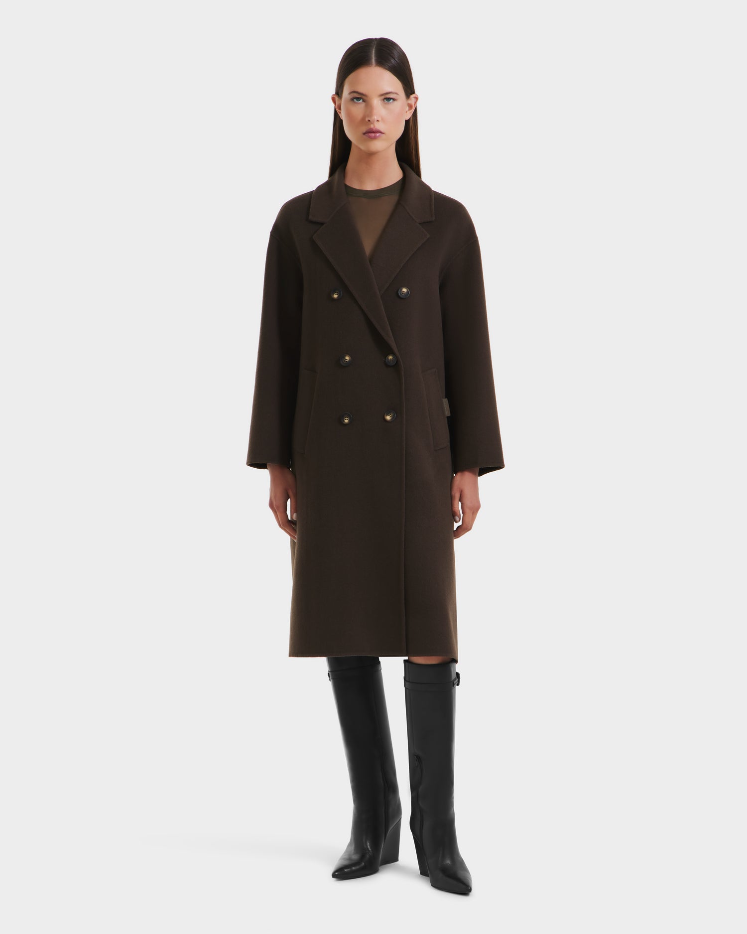 A woman stands facing forward in a long, dark green Rudsak JADE - 8125673 Army womens wool overcoat with gold buttons, black knee-high boots, and a neutral expression, set against a plain white background.