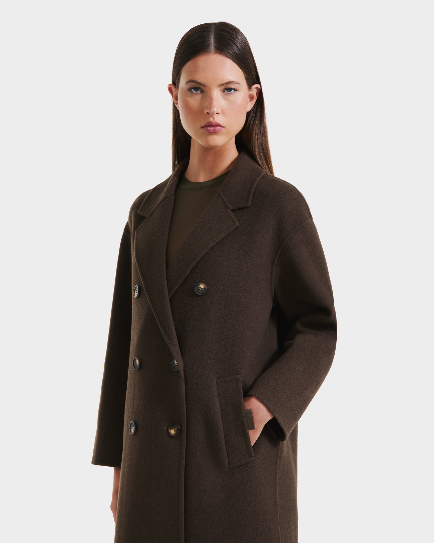 A woman with straight dark hair wears the Rudsak JADE - 8125673 Army women’s wool overcoat, a long double-breasted style with front pockets, over a dark top against a plain white background.