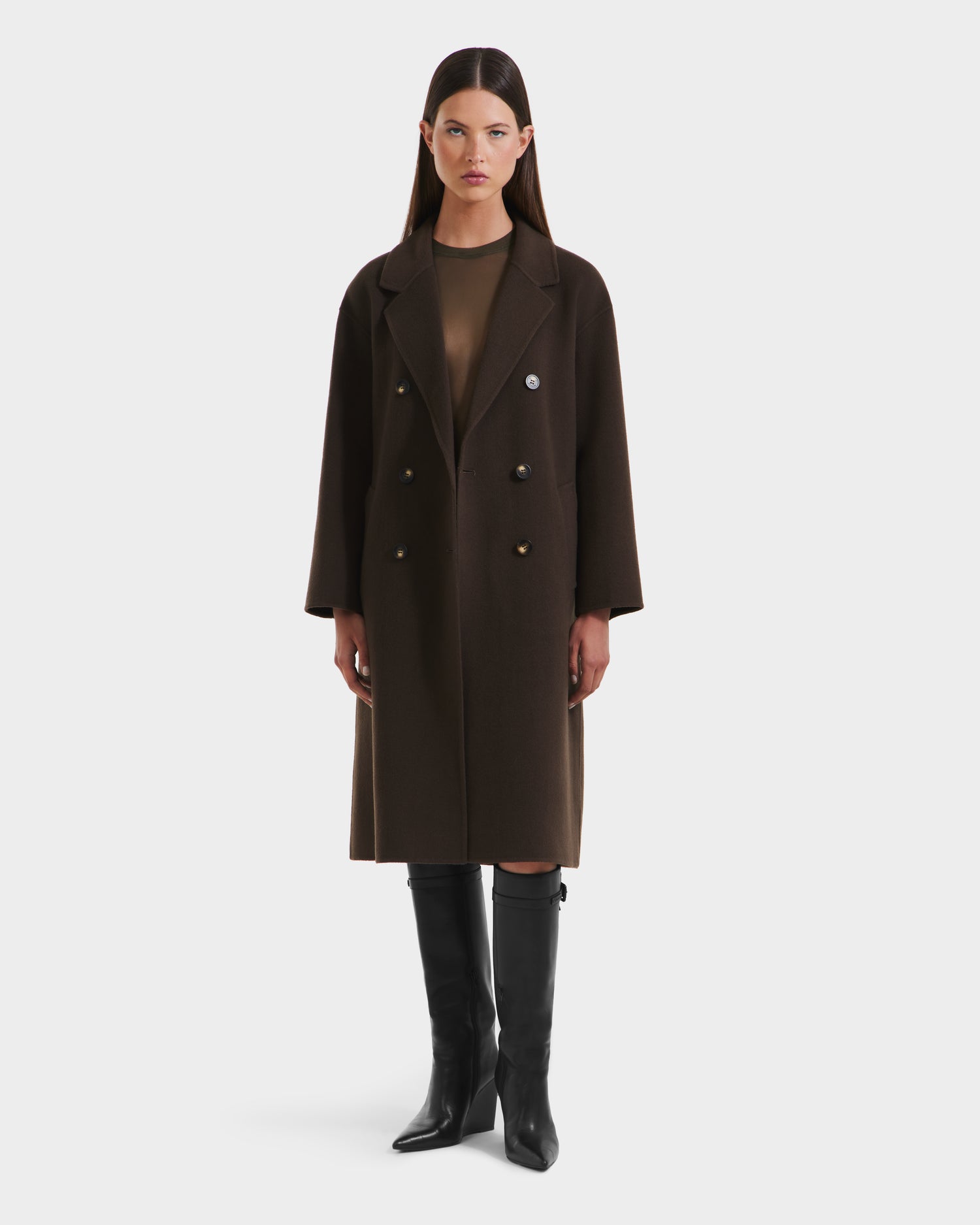 A woman with straight, dark hair and a neutral expression faces forward in a Rudsak JADE - 8125673 Army double-breasted coat over a sheer brown top, paired with knee-high black boots against a plain white background.