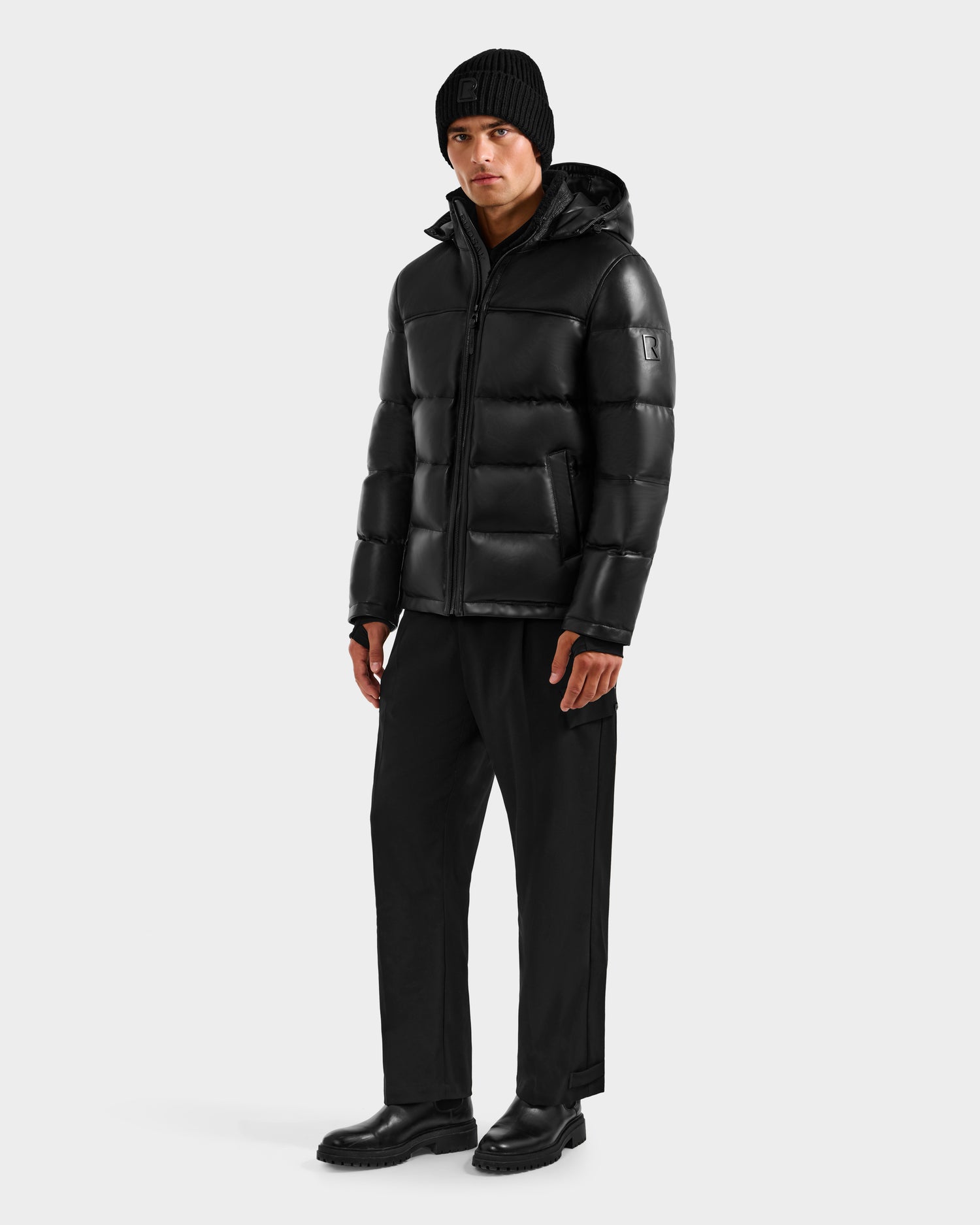 A person wearing the Rudsak JAMESON - 6125678 Black quilted leather down jacket stands facing forward against a plain white background.