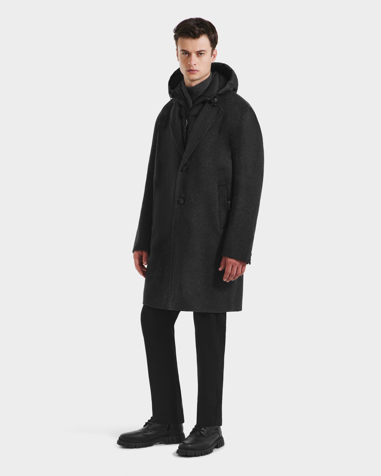 A man faces forward in the Rudsak JEREMIAH - 6125509 Grey wool-blend hooded coat, styled over a black outfit and shoes—a cold-weather essential—set against a plain white background.