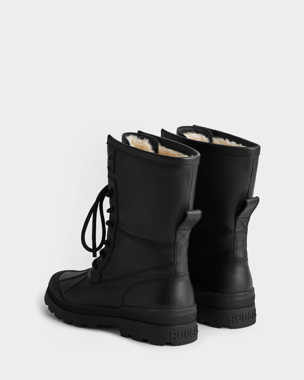 The Rudsak JESI - 8225026 Black winter boots feature black lace-up design, thick soles, and visible white fleece lining. They are shown on a white background, angled to display the back.