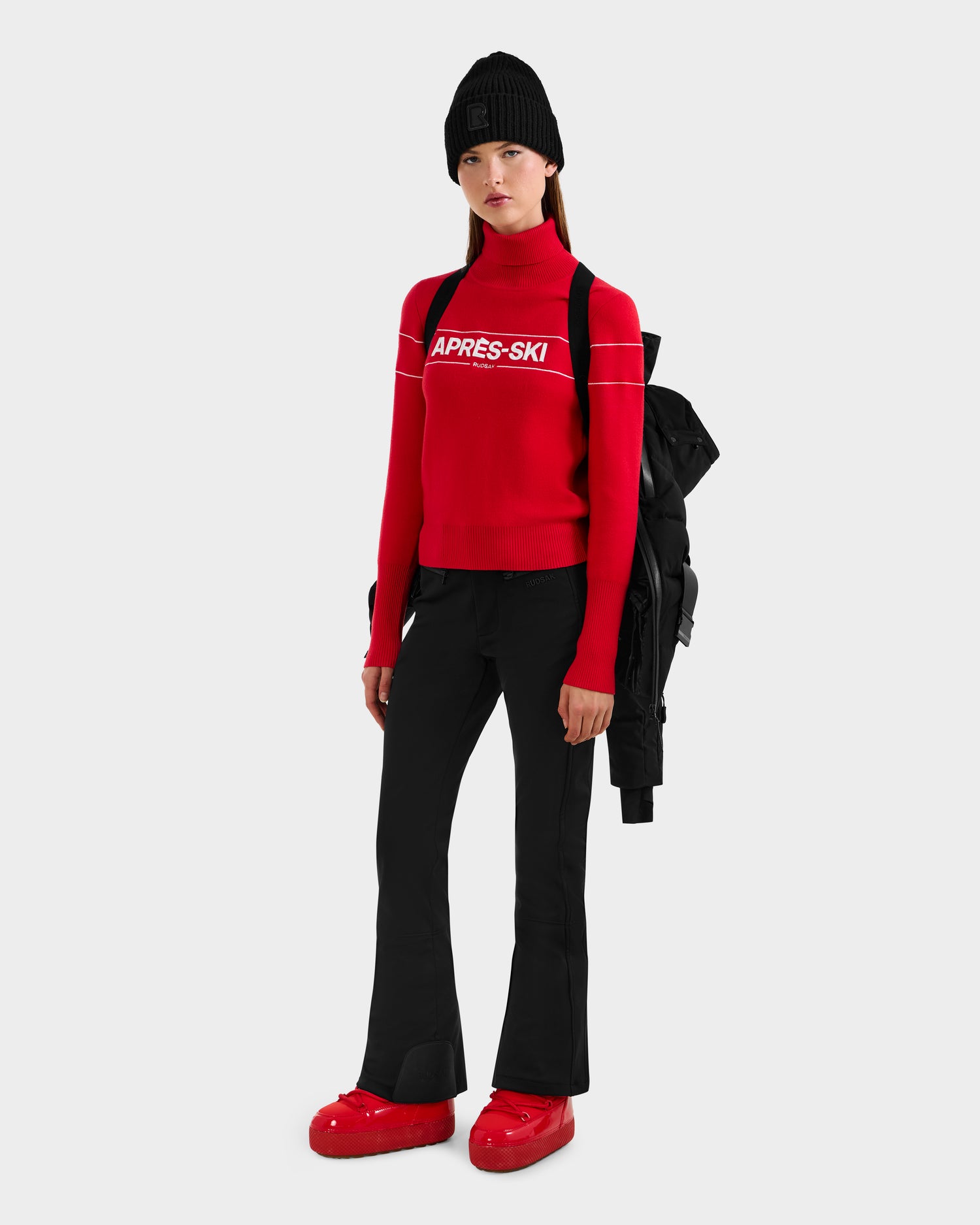 A woman in a black hat and red sweater is ready for winter, showcasing the Rudsak JOANNA - 8124788 Black women's down ski jacket with removable belt.