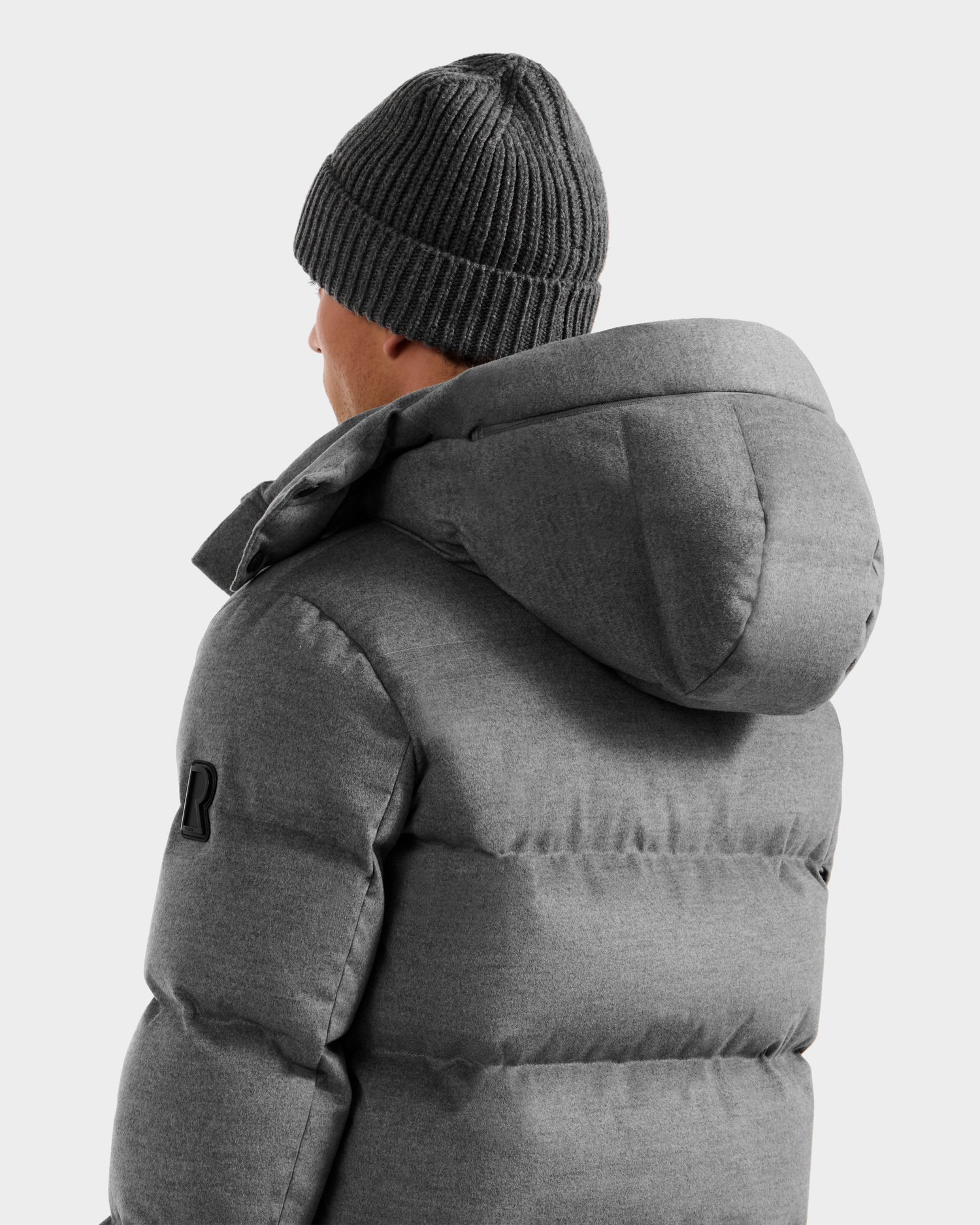 A person models the Rudsak JOEL W - 6125683 Heather Charcoal men's puffer, featuring a removable hood, showing the back and side against a plain light background.