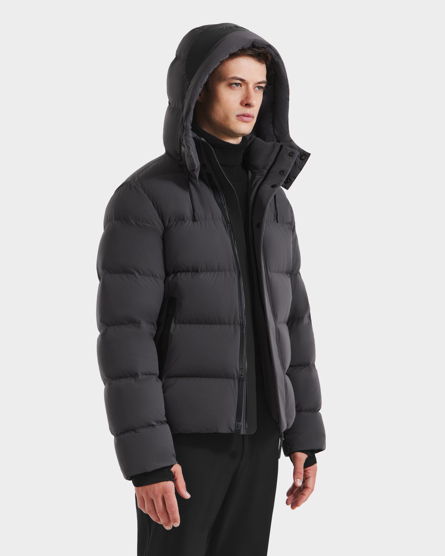 A person models the Rudsak JOEL - 6124605 Grey men’s puffer jacket with a weather-resistant shell and hood, standing against a plain white background, looking to the side.