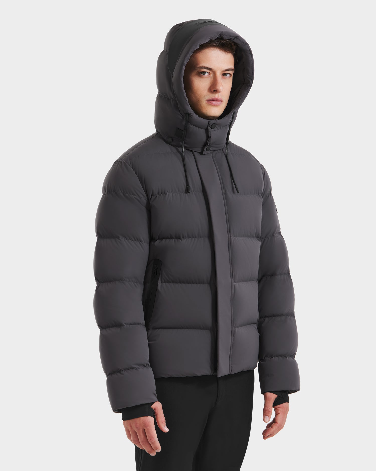 A person wearing the Rudsak JOEL - 6124605 Grey men's puffer jacket with a high collar and weather-resistant shell stands against a plain white background.